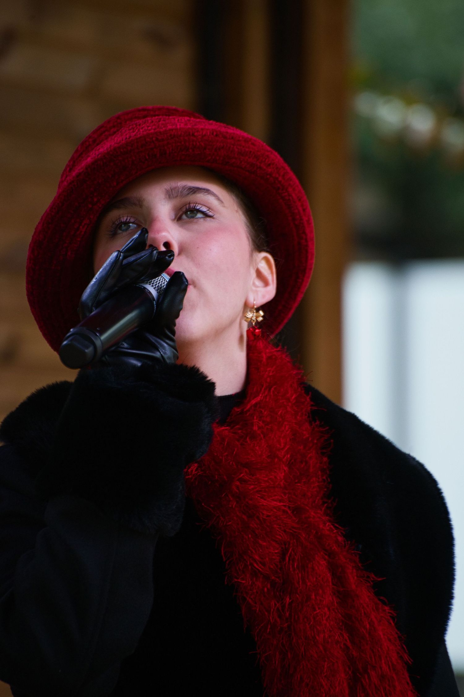 Performer in red hat and black gloves sings into microphone during winter performance.
