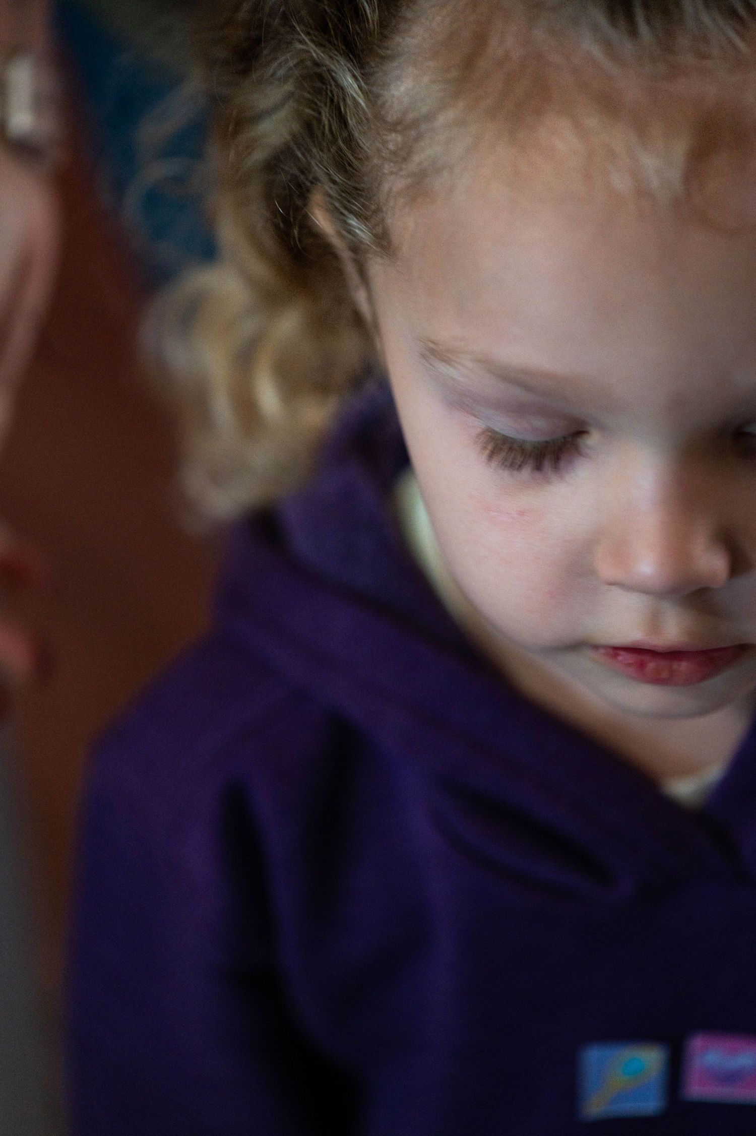 Child in purple hoodie looking down with soft lighting on their face.