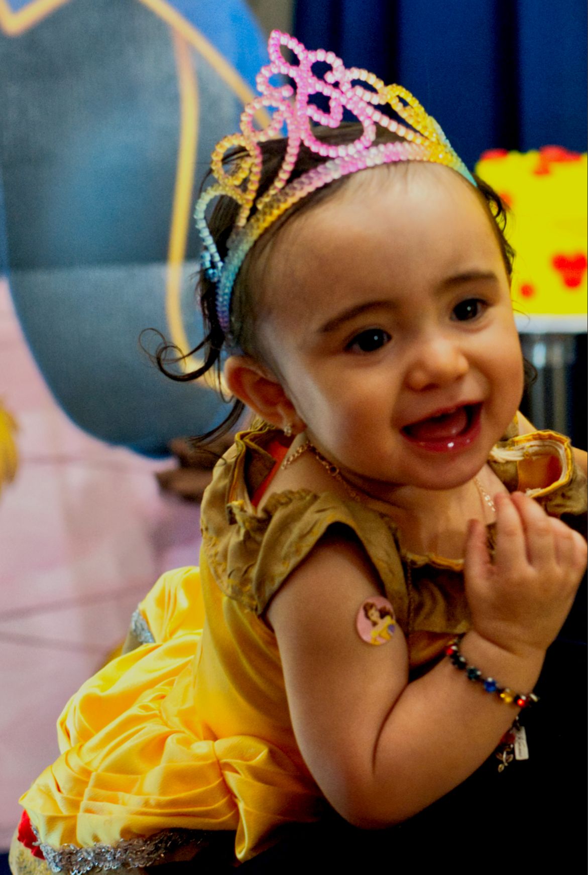 A small child wearing a sparkly tiara and yellow dress smiles during a celebration.