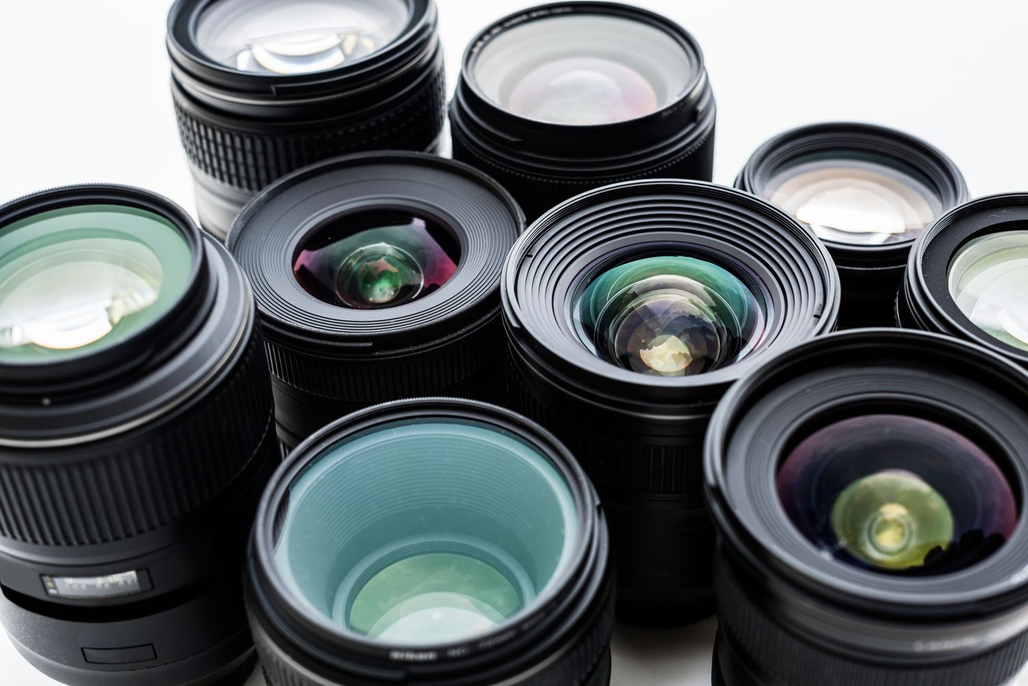 A collection of professional camera lenses with glass elements showing various focal lengths arranged on white background.