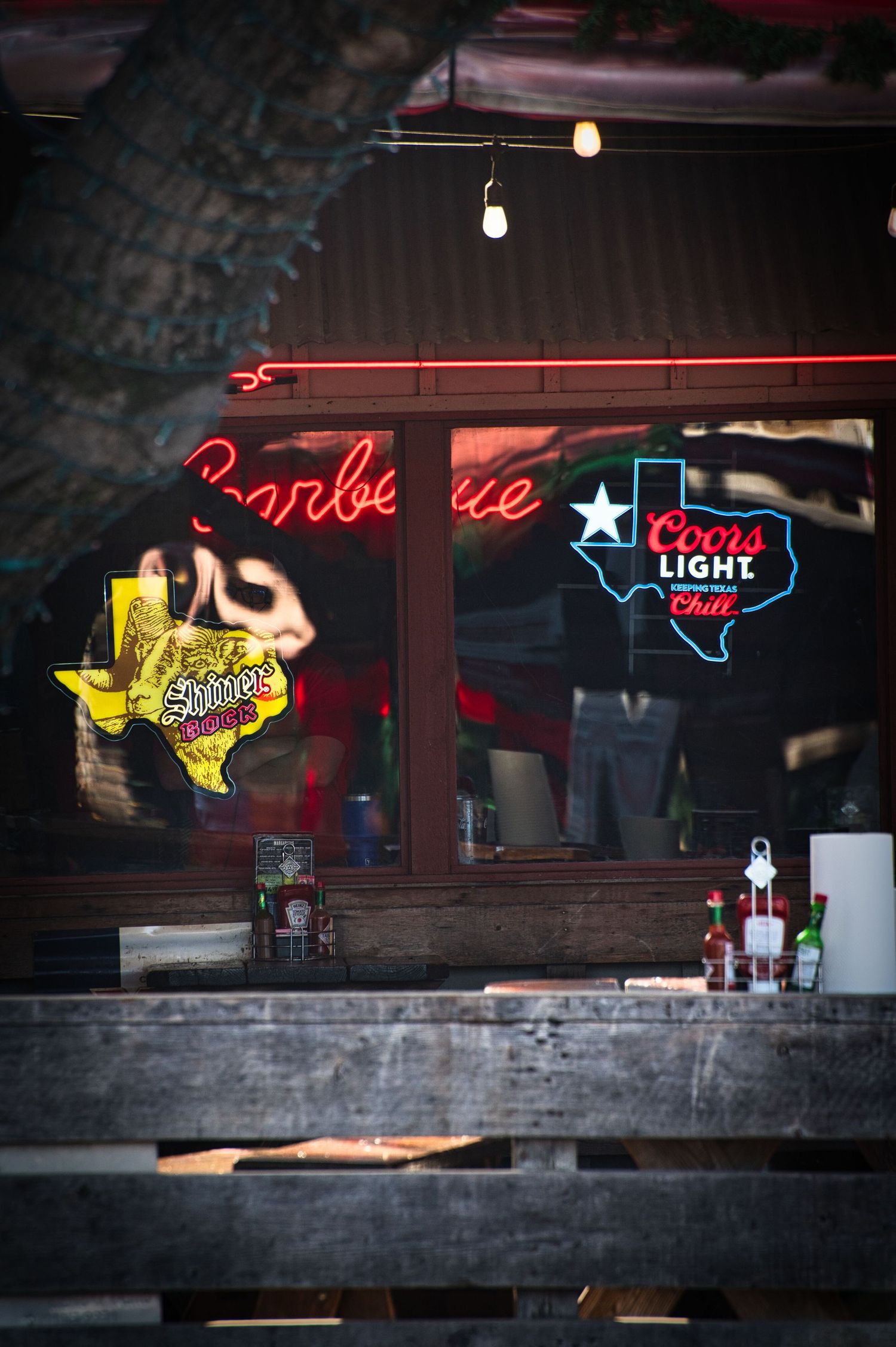 Neon Texas signs and Coors Light logo illuminate a bar window at night.