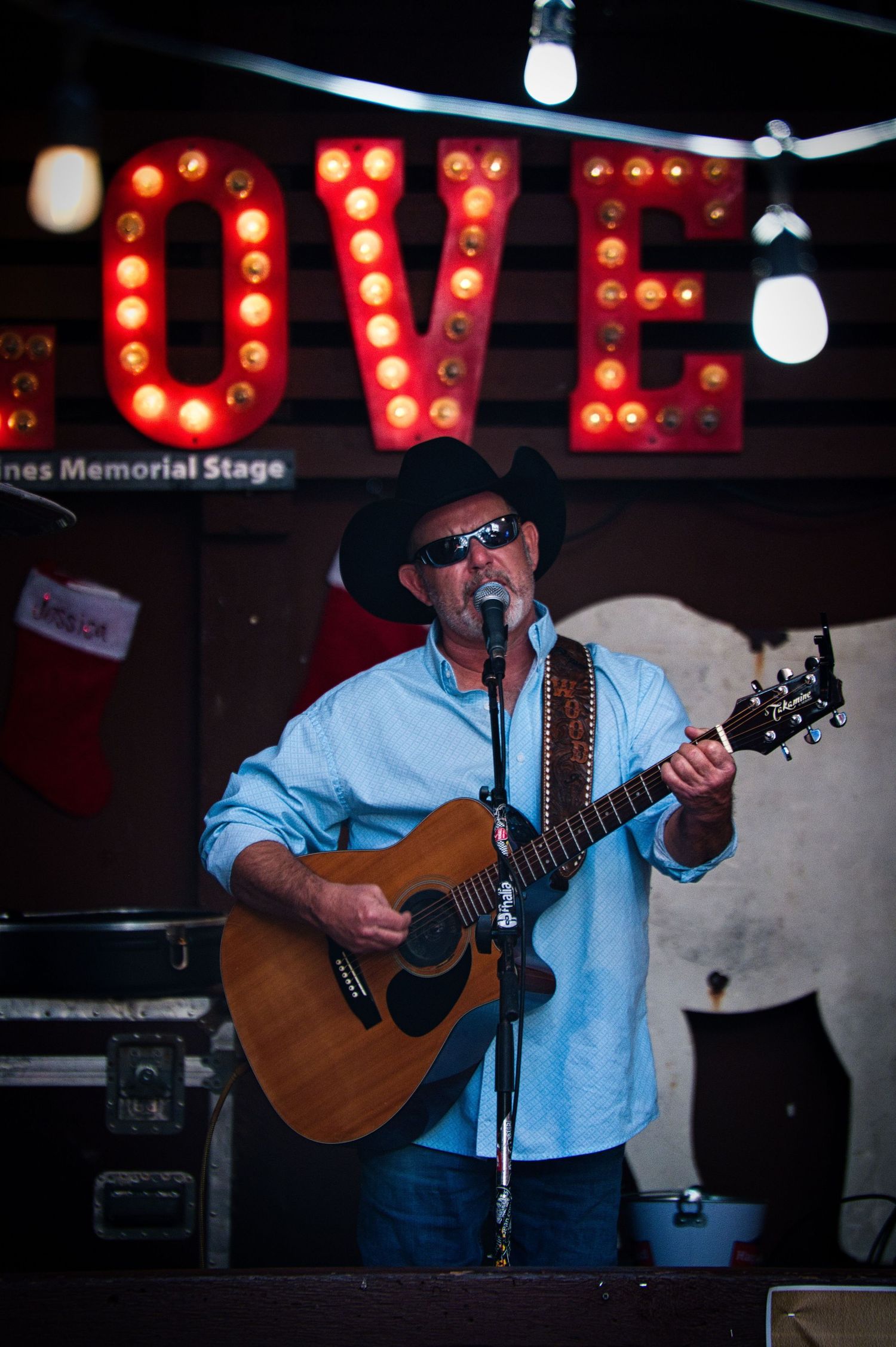 Country musician performs with acoustic guitar under illuminated LOVE sign.