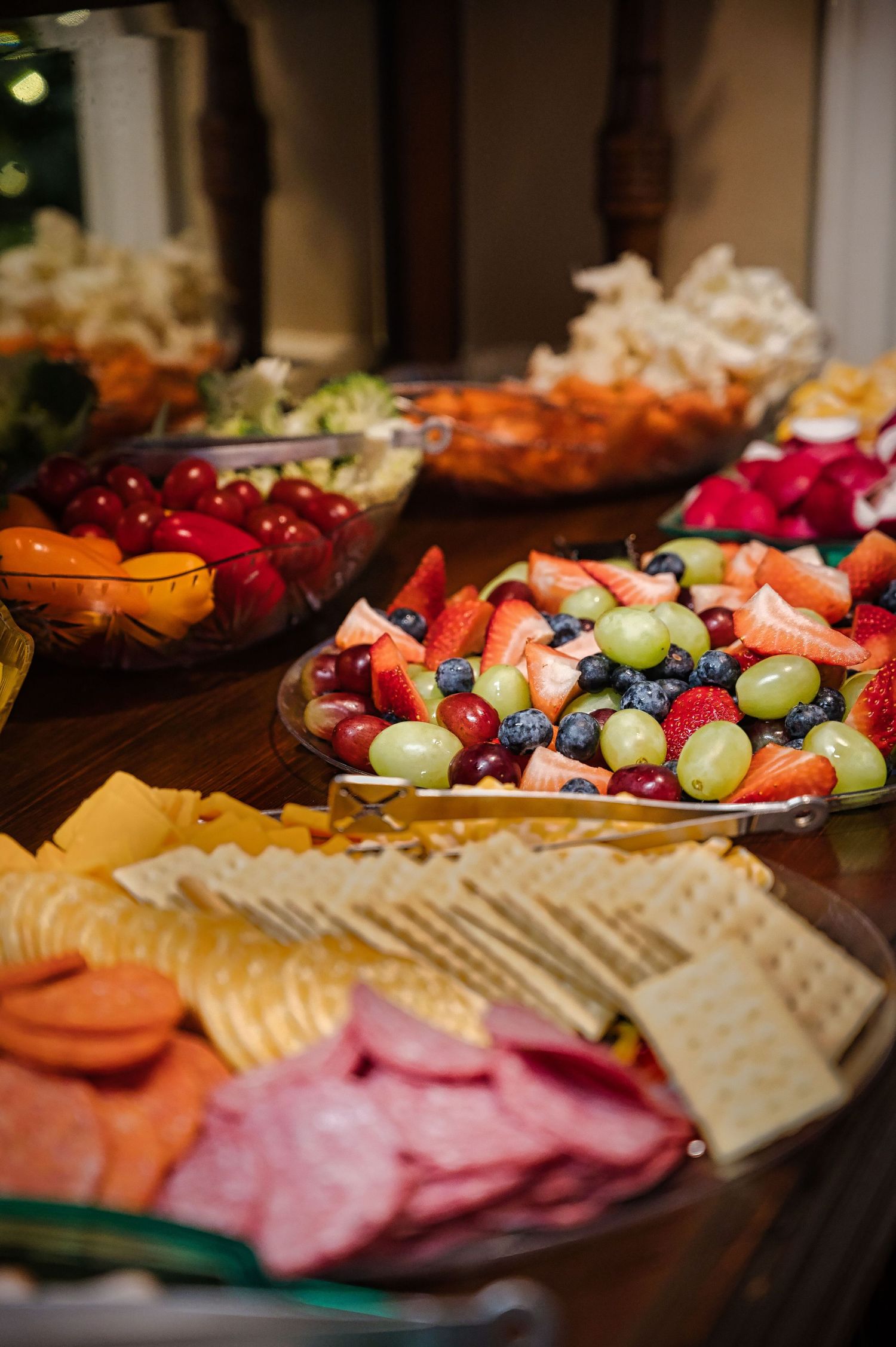 Colorful party platter with fresh fruit, crackers, and deli meats arranged on a wooden table.