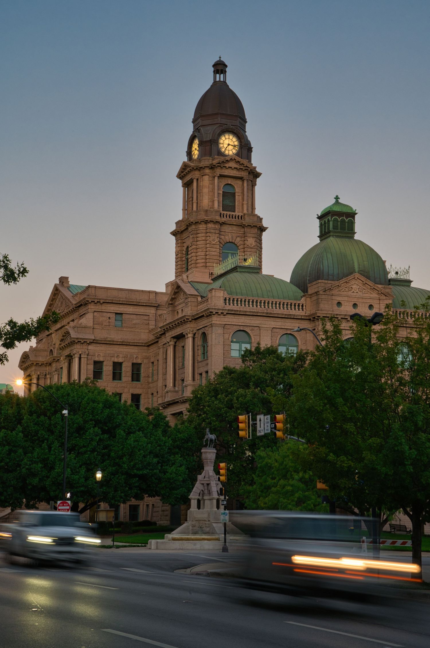 Historic courthouse building with clock tower and copper dome captured at dusk with motion blur of passing cars.