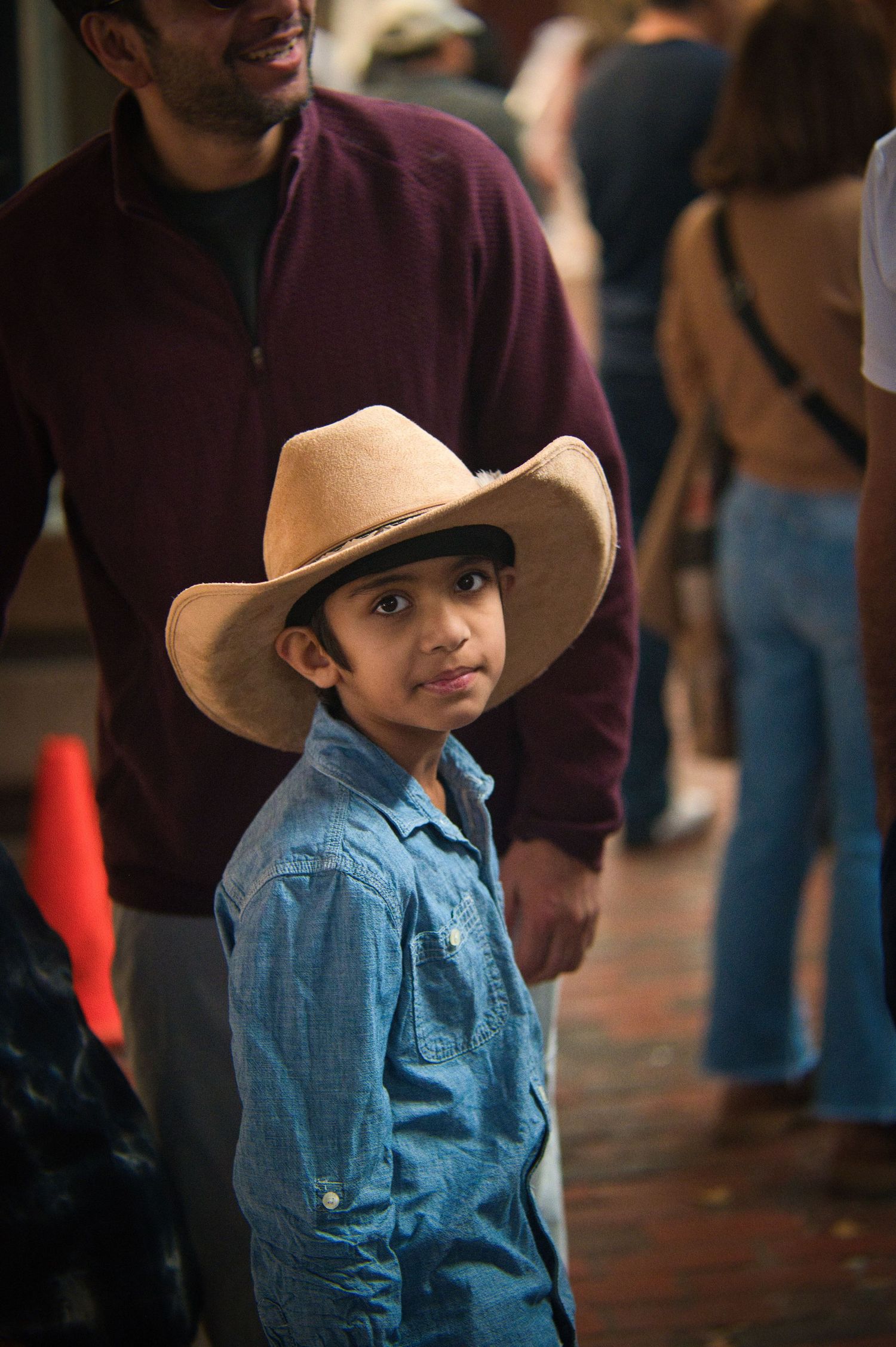 A young person in a cowboy hat and denim shirt looks to the side in an indoor setting.