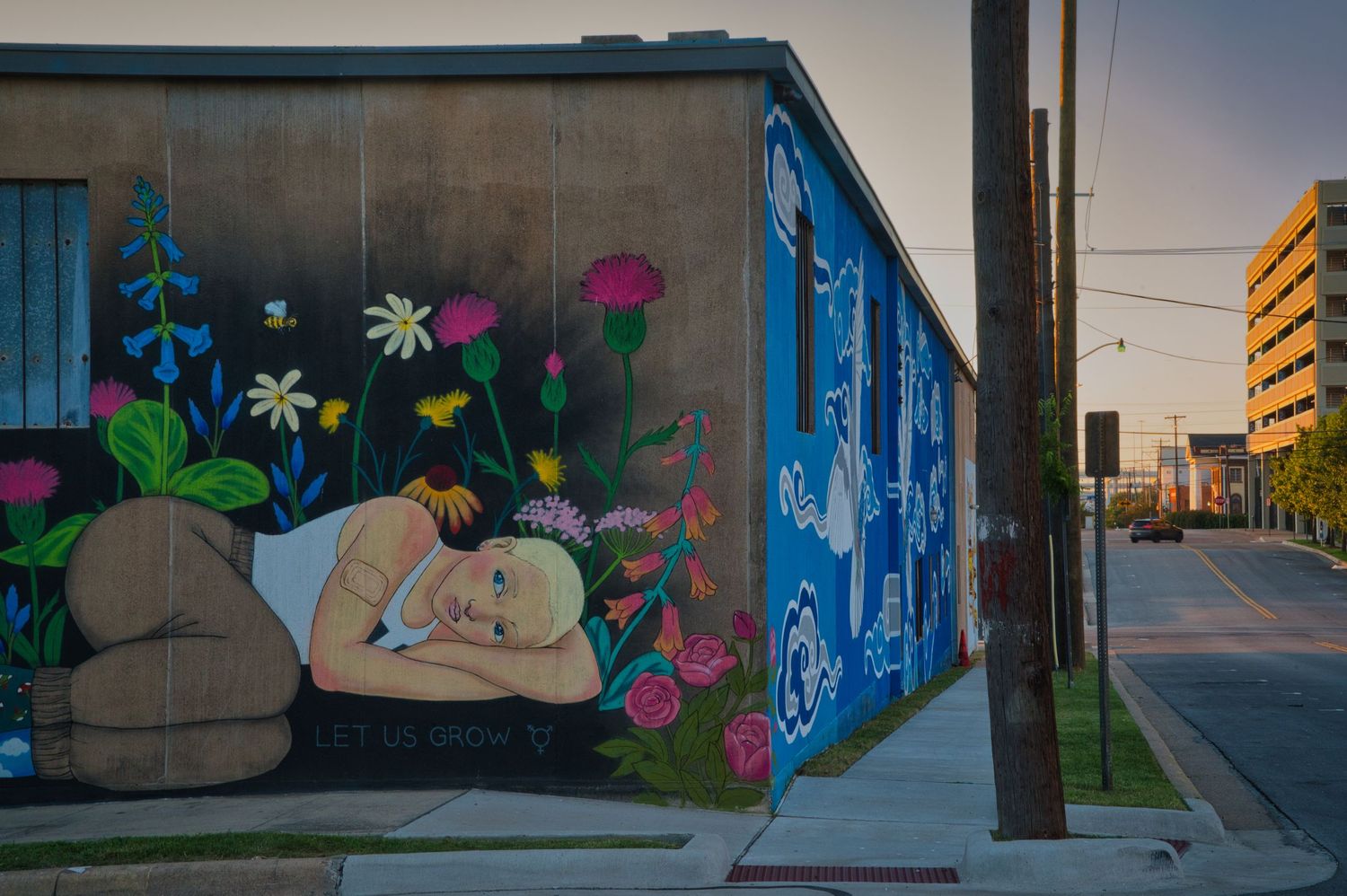 A colorful street mural featuring flowers and a sleeping figure decorates the corner of a building.