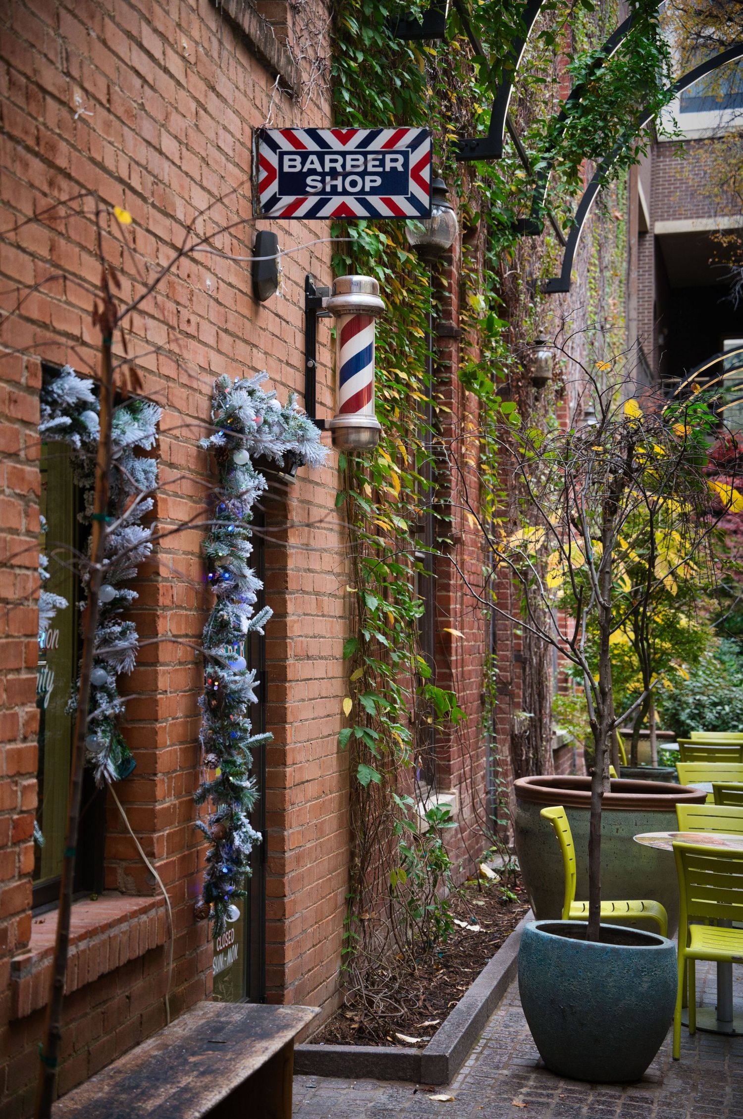 Traditional barber shop pole and sign mounted on brick wall with climbing vines and flowers.