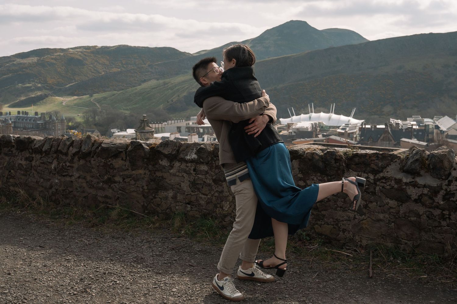 Couple embracing after proposal with Edinburgh skyline