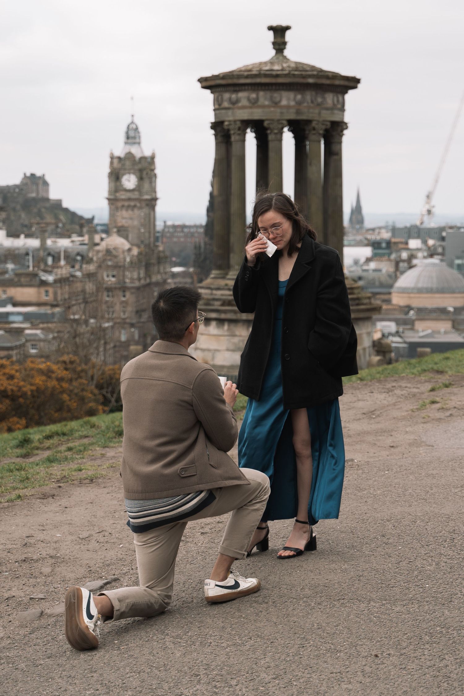 Couple embracing after proposal with Edinburgh skyline