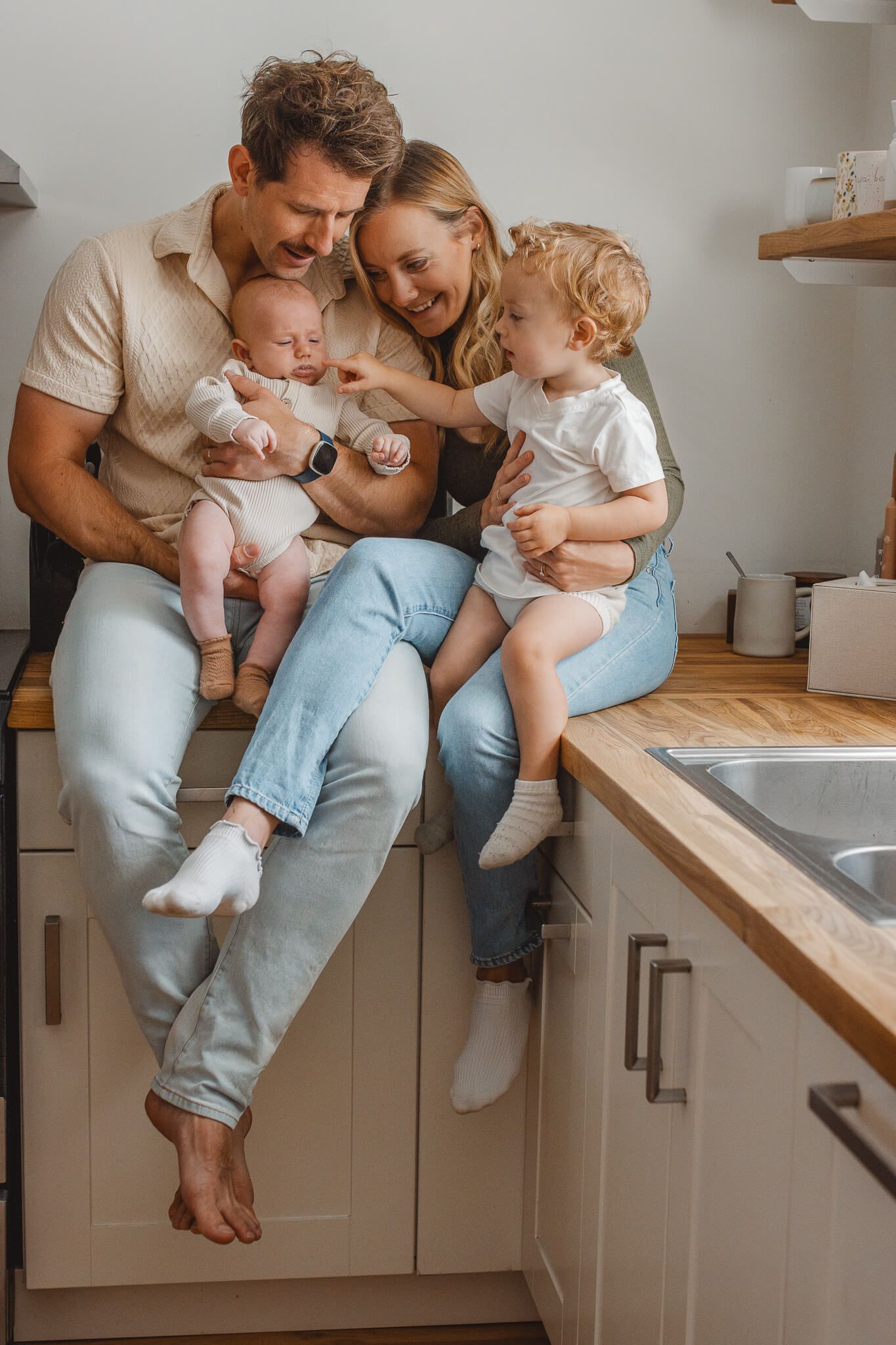 Family sits together casually on kitchen counter, sharing a tender moment at home in warm lighting.