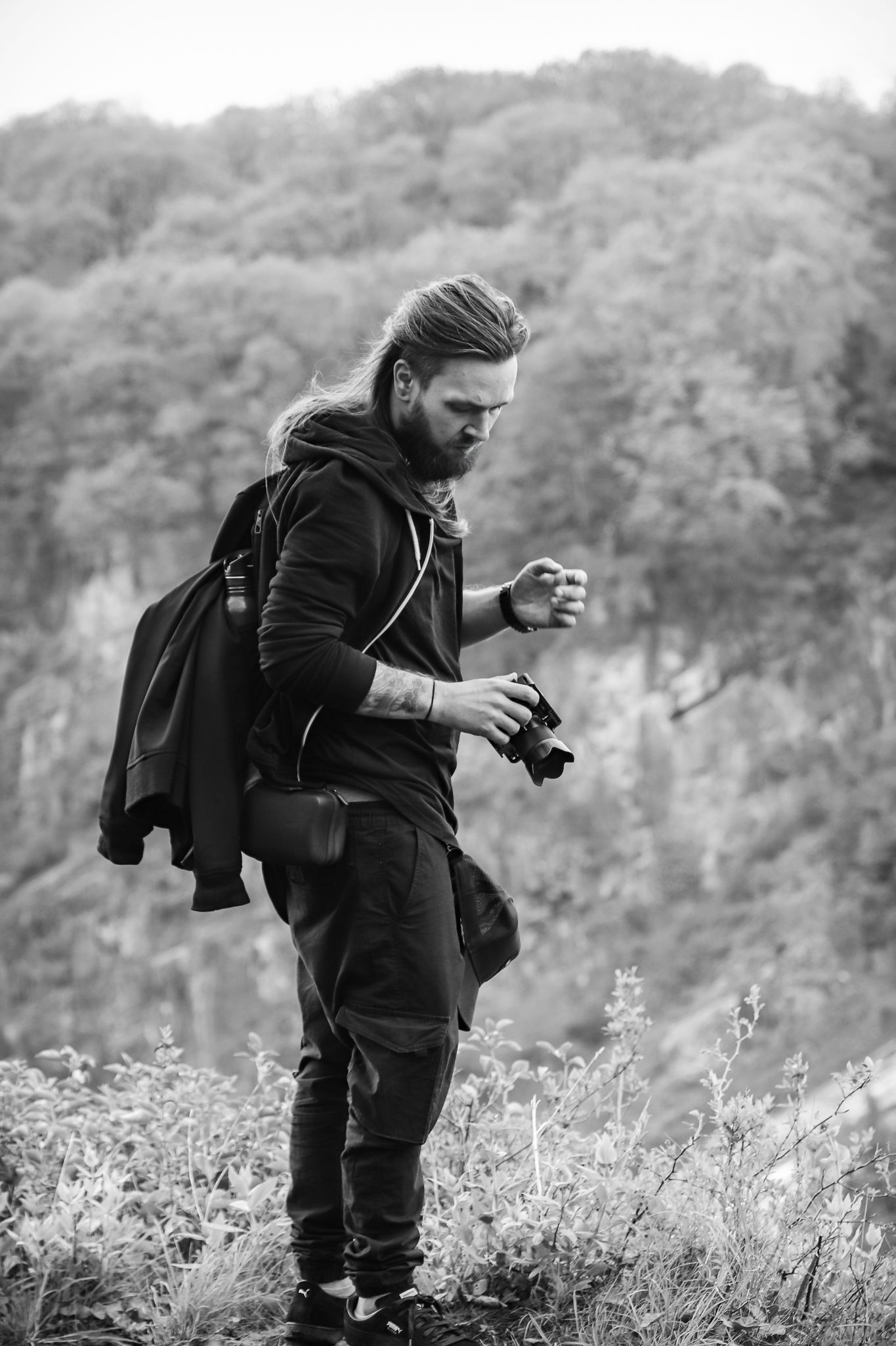 A photographer in black attire crouches in a field of wildflowers while taking macro photographs in nature.