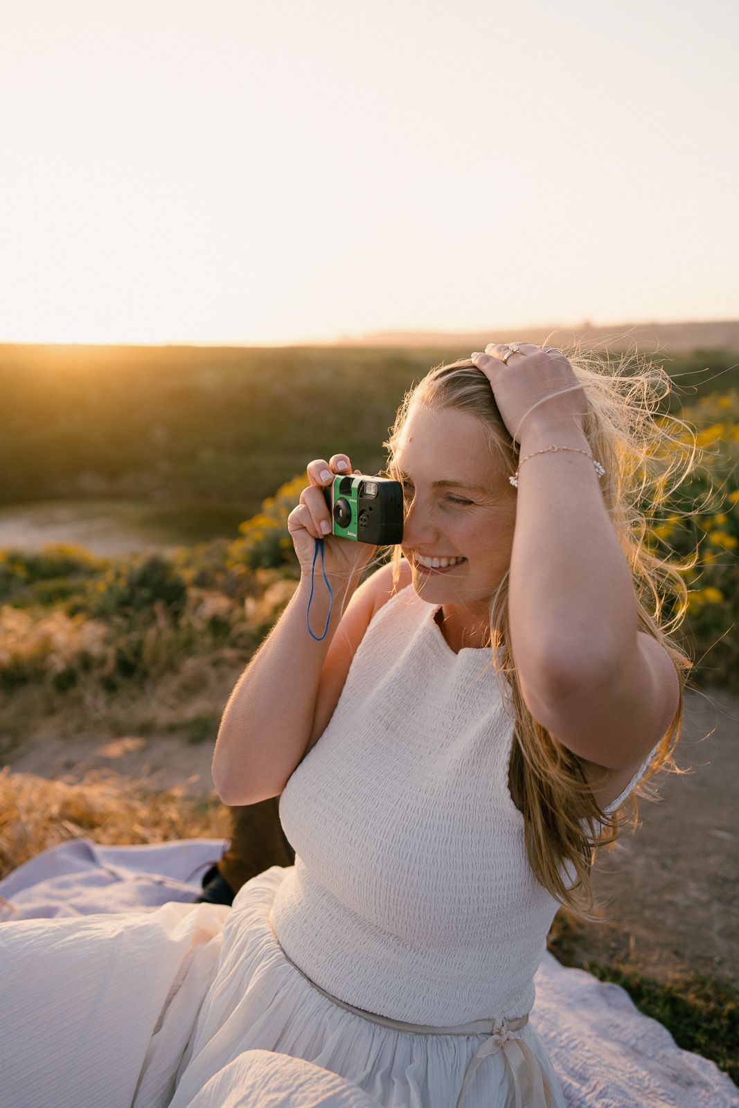 Person taking photos with vintage camera while sitting outdoors during golden hour sunset.