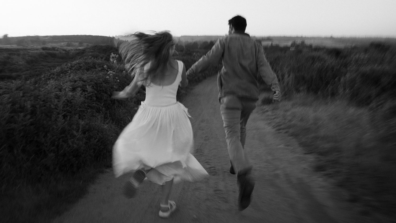 A romantic couple runs and dances together along a scenic country path at sunset.