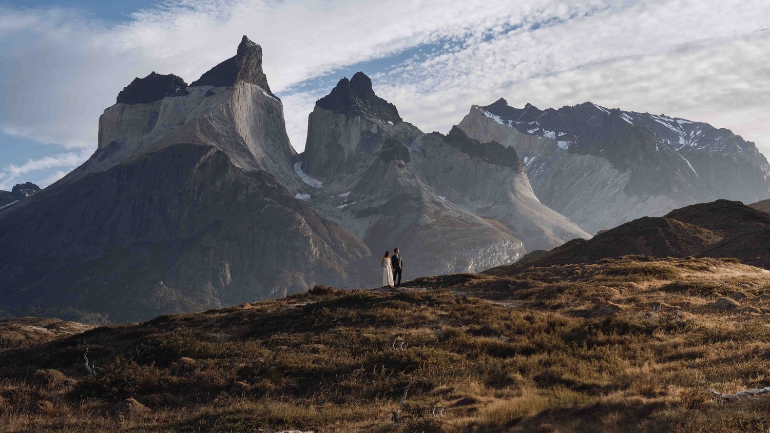 A silhouetted figure stands on a hilltop overlooking the majestic peaks of Torres del Paine in Patagonia.