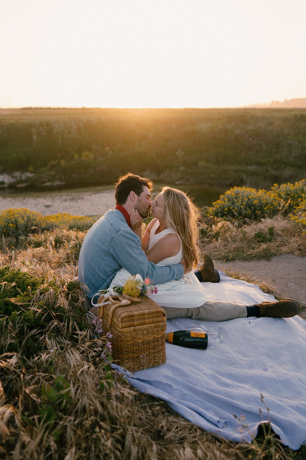 Romantic sunset picnic on a blanket with wicker basket and golden light glowing across scenic natural landscape.