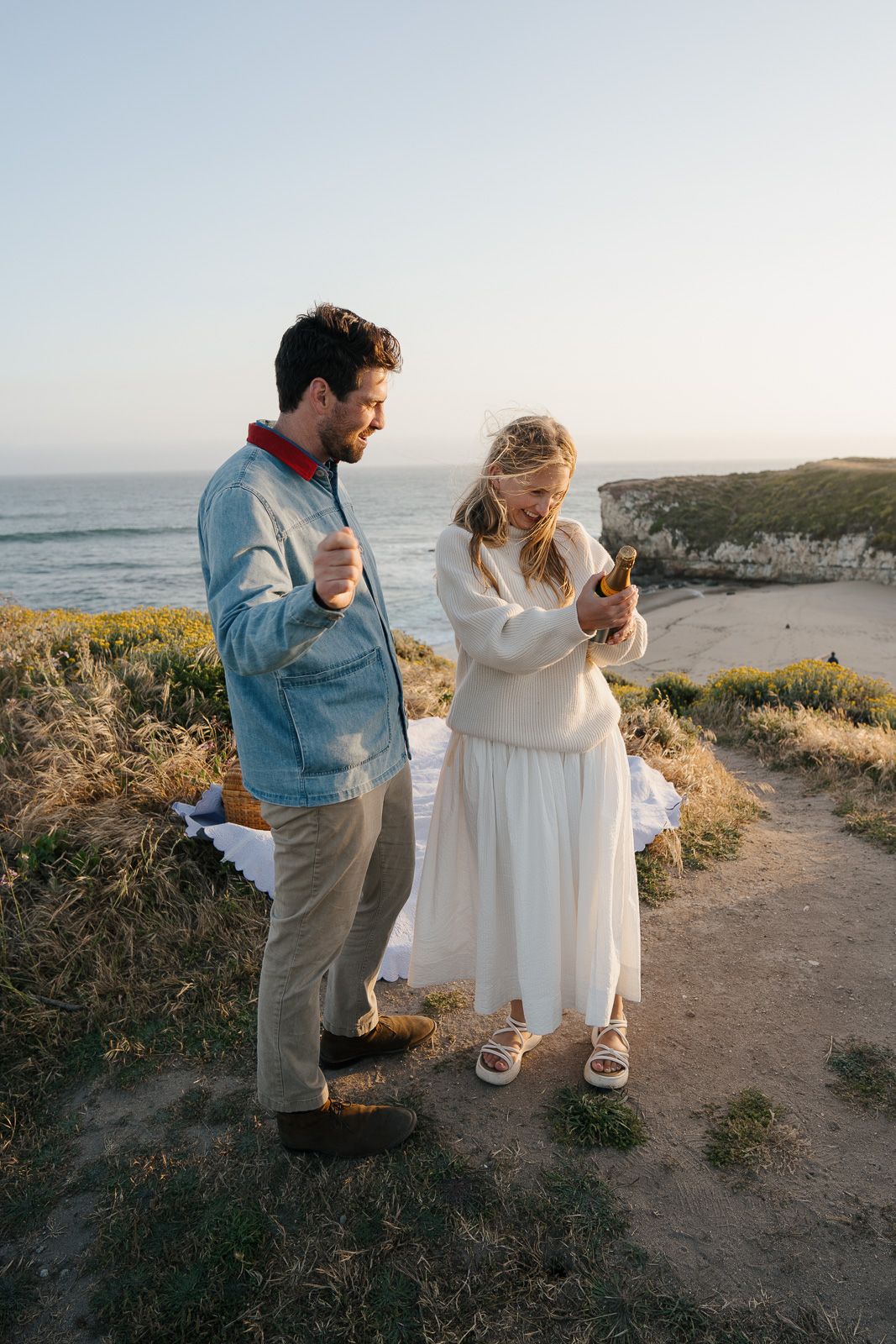 A couple shares a romantic moment on a coastal cliffside path during golden hour.