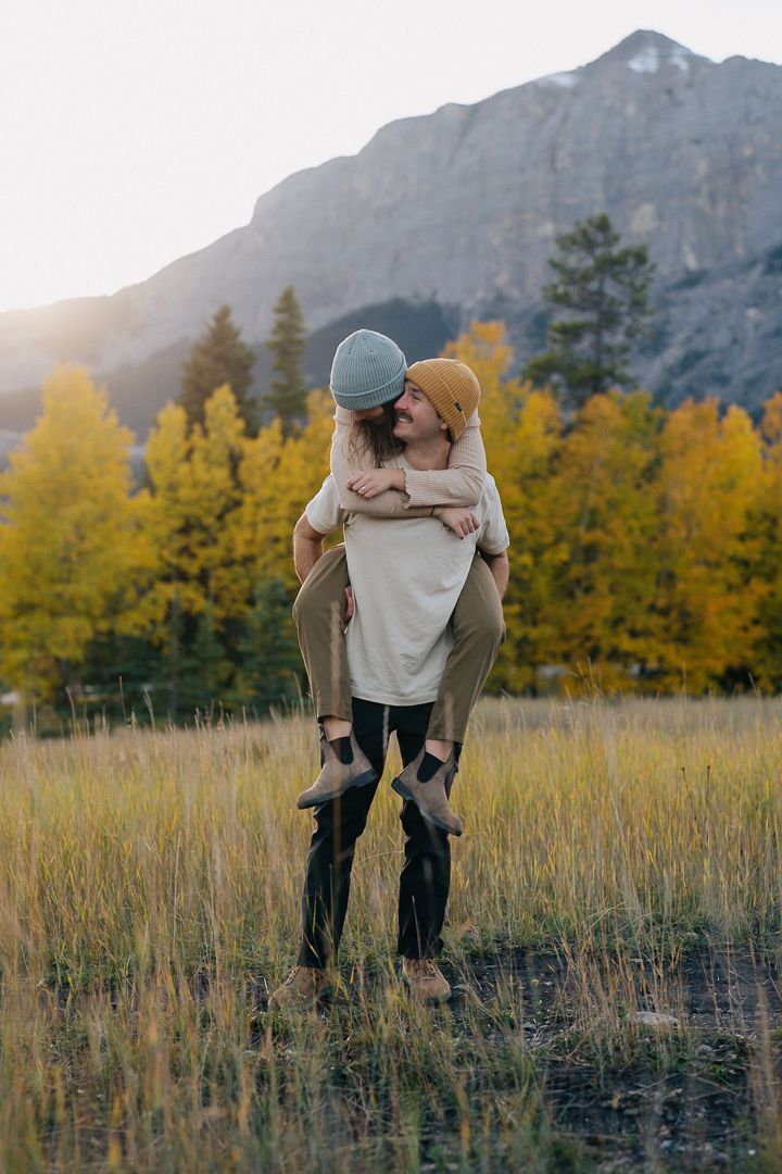 Silhouette of a couple embracing in a field with autumn trees and mountain backdrop at sunset.