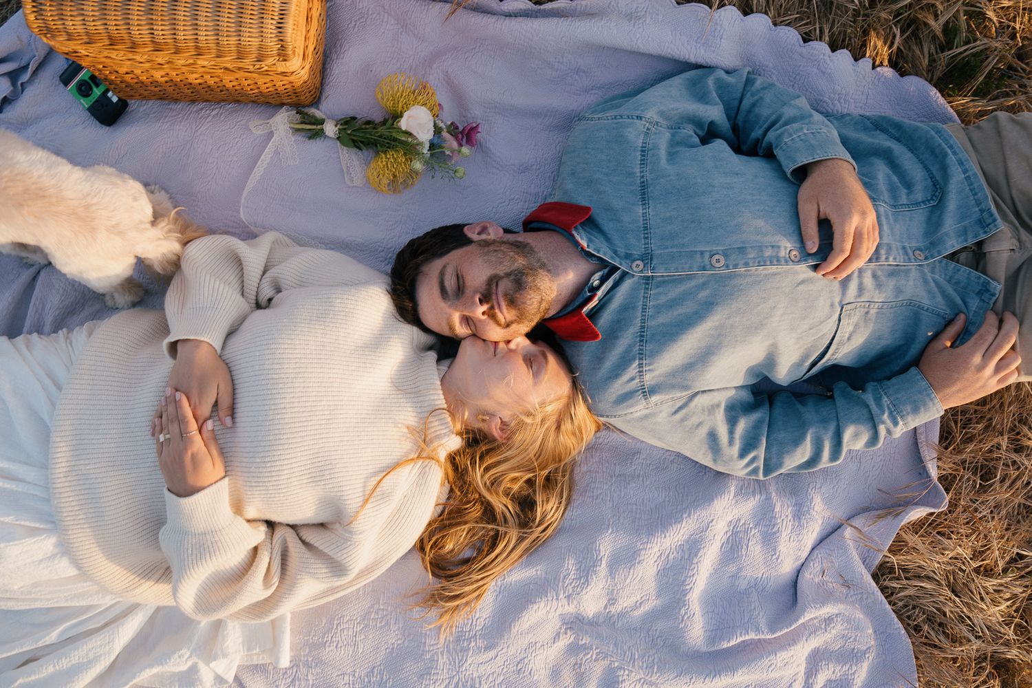 A picnic basket sits beside someone reclining in a grassy field during golden hour.