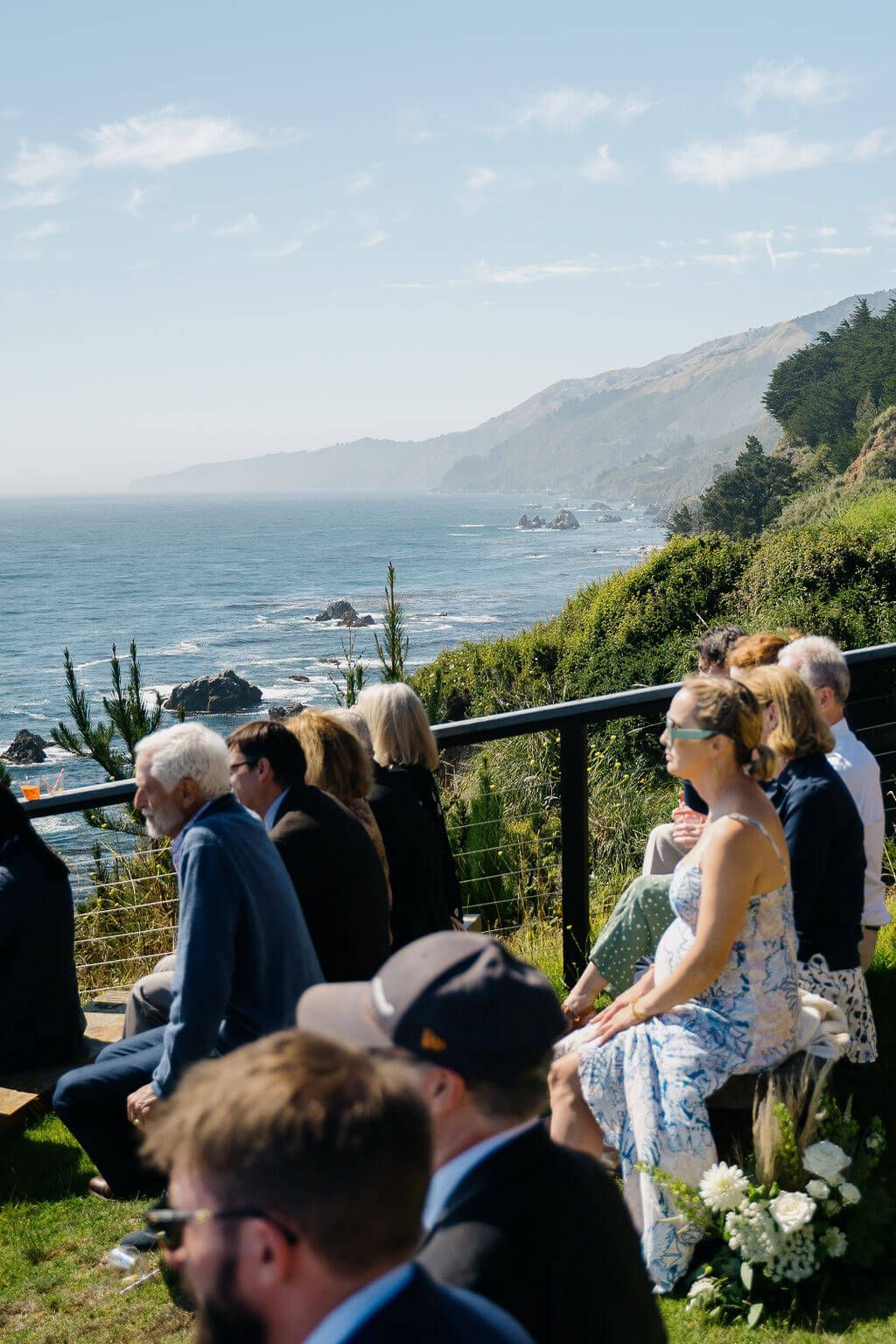 Ocean view wedding ceremony overlooking dramatic Pacific coastline with mountains and rocky cliffs in the background.