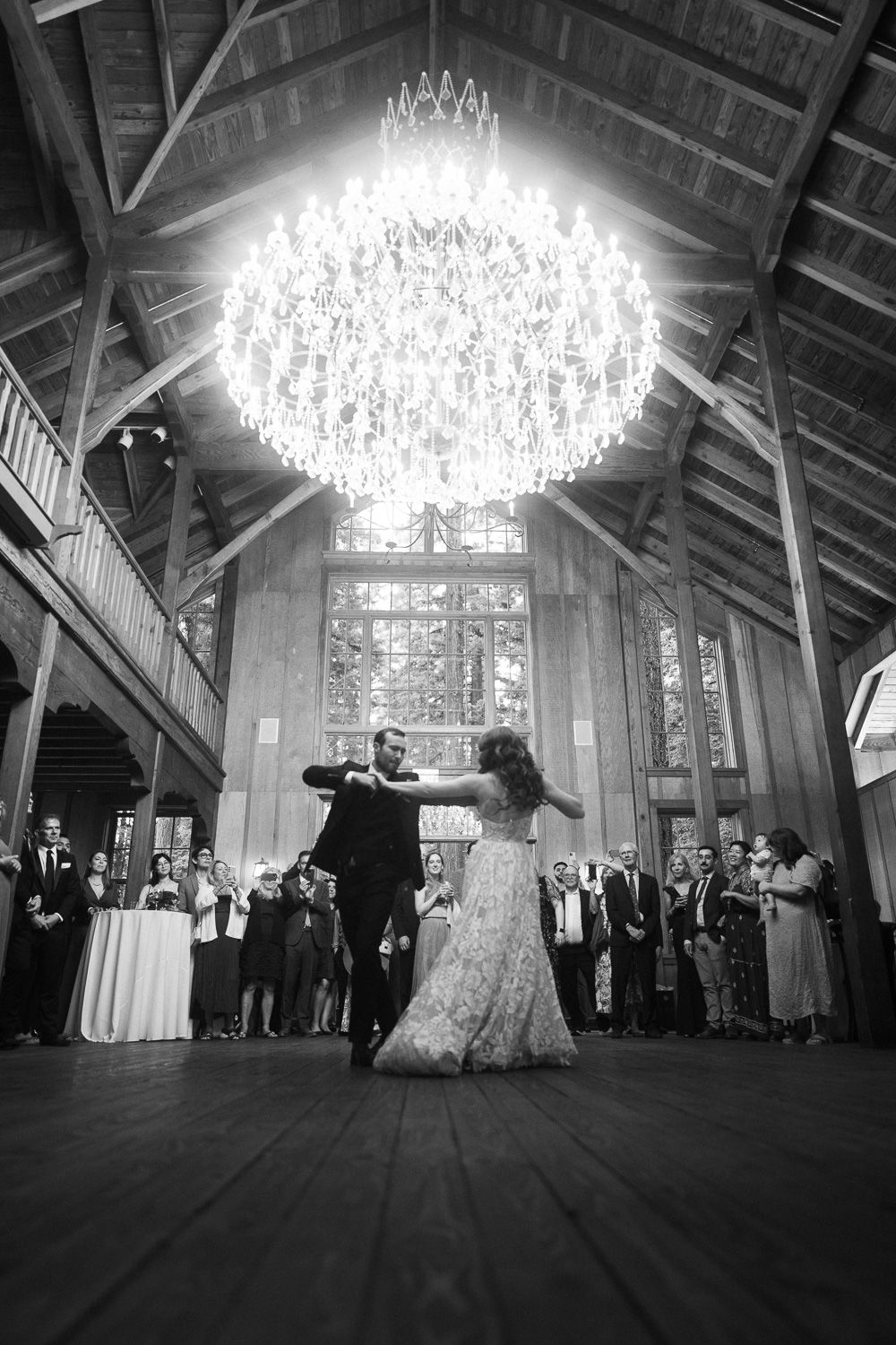 A sequence of black and white ballroom dance photos under a grand chandelier in a rustic wooden barn venue.
