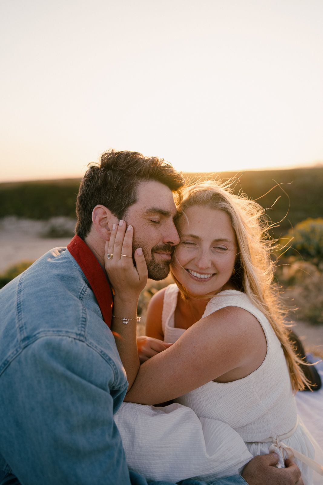 A couple shares a tender moment while embracing outdoors during golden hour sunset, with warm backlighting.
