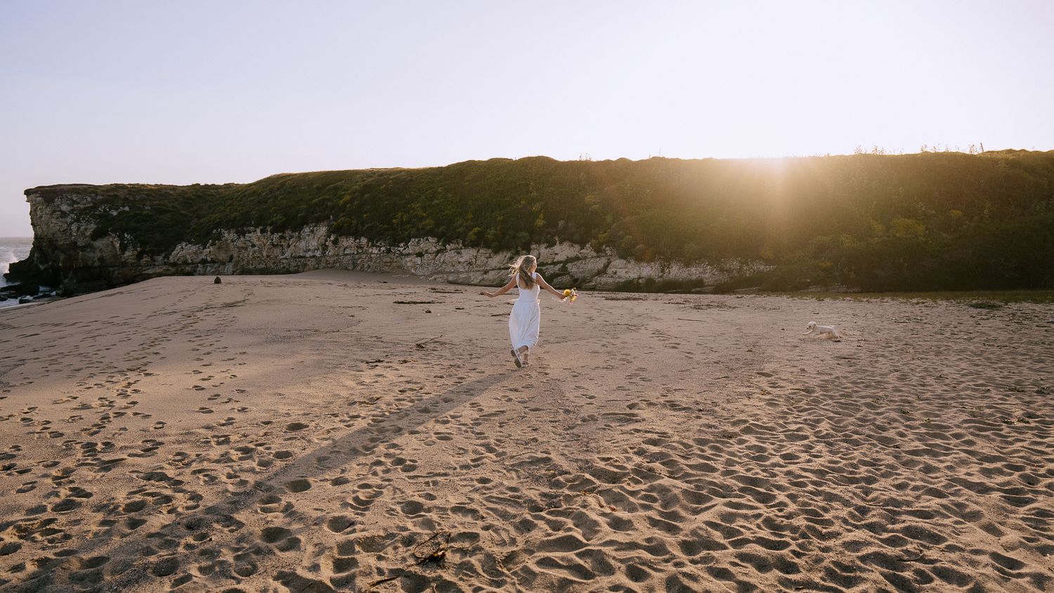 Scenic desert landscape at sunset with warm orange light illuminating sandy dunes and rock formations in the distance.