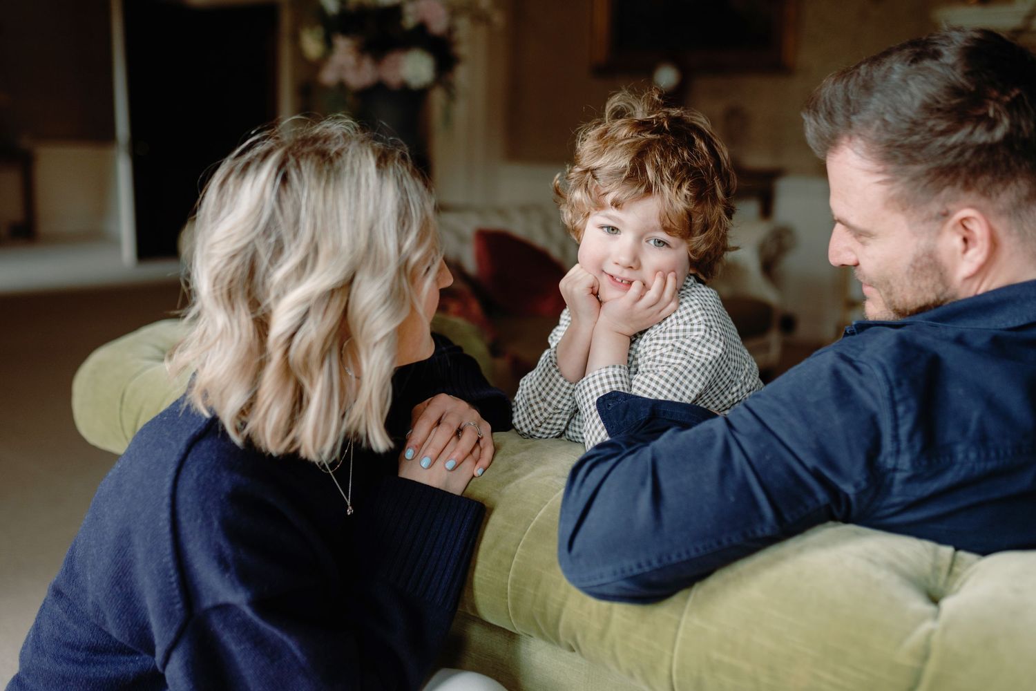 Parents and toddler share playful moment together while relaxing on green couch at home.