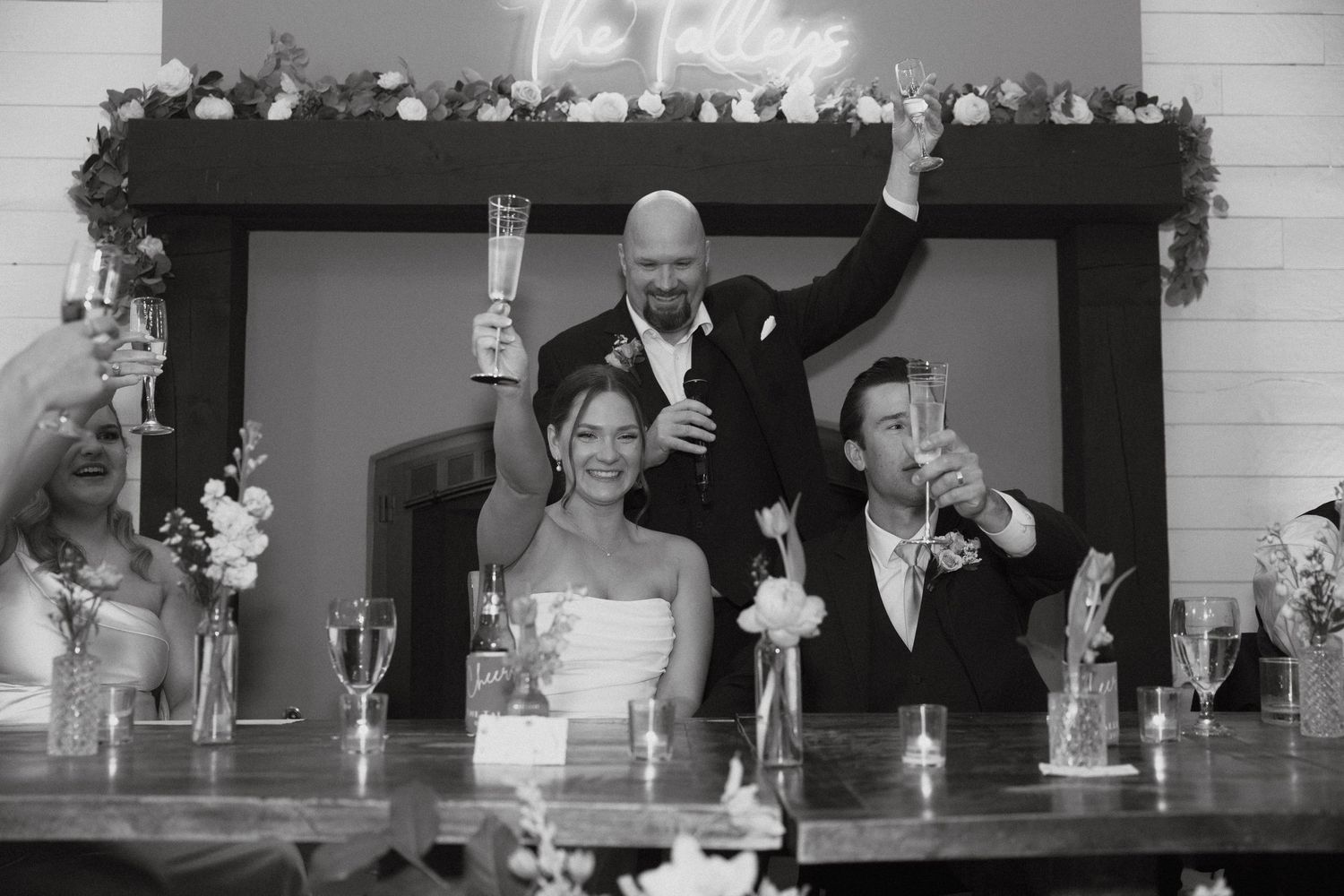 Wedding party members celebrate at a reception table decorated with floral garlands.