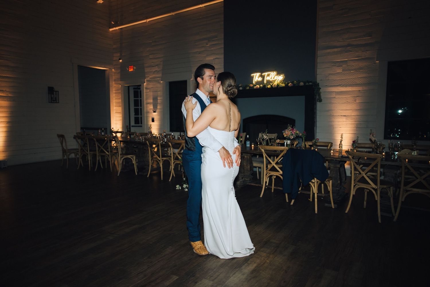 A couple shares their first dance at a wedding reception in a dark venue illuminated by warm ambient lighting.