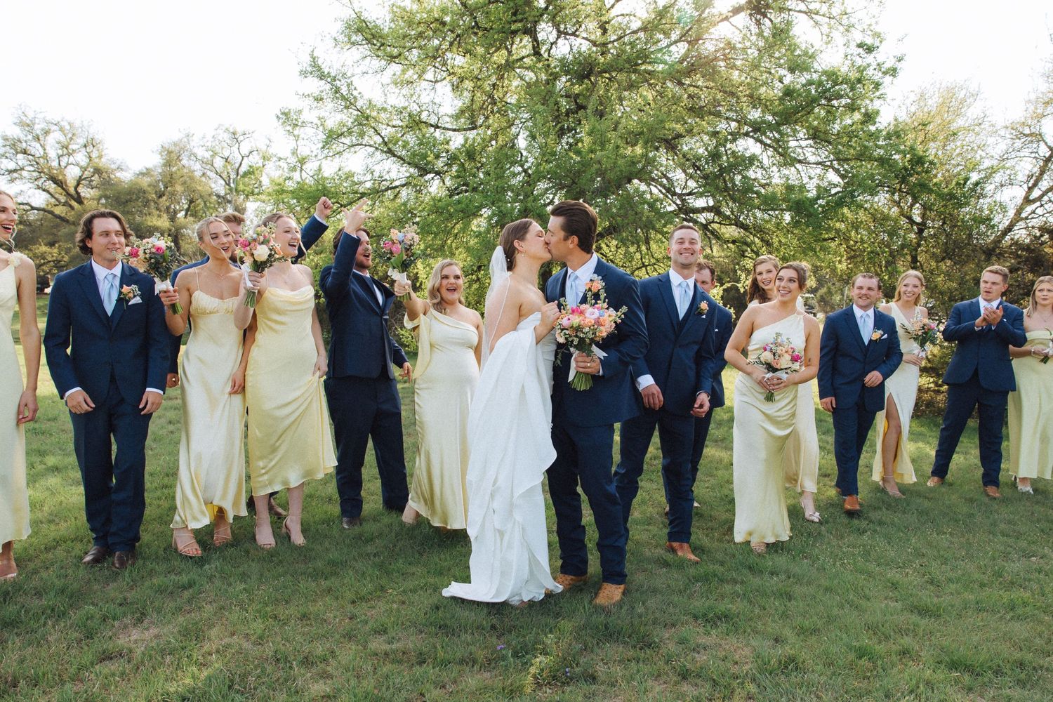 Wedding party stands in a line on grassy lawn with yellow and navy color scheme for bridal portraits.