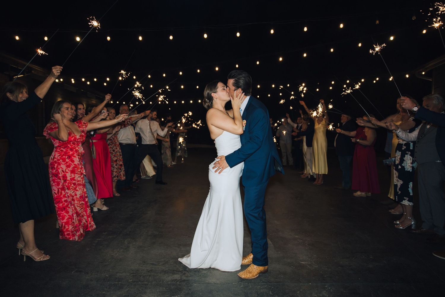 Wedding reception dance floor at night with string lights illuminating guests and newlyweds dancing under the stars.
