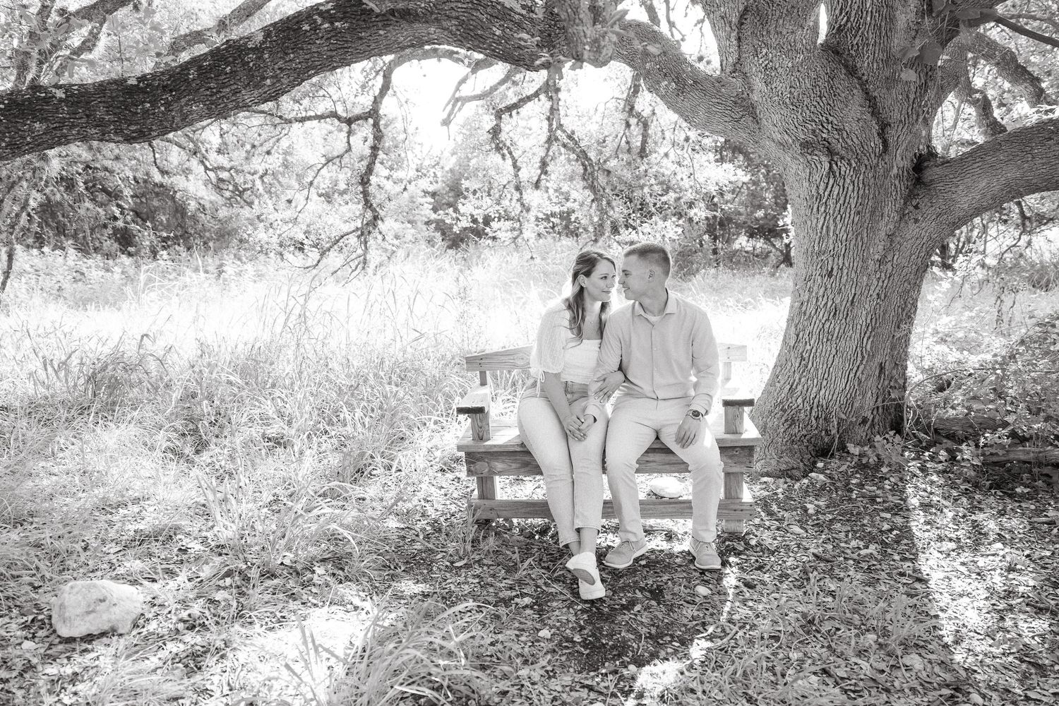 A cozy outdoor seating area with white Adirondack chairs arranged beneath a sprawling tree in a serene garden setting.