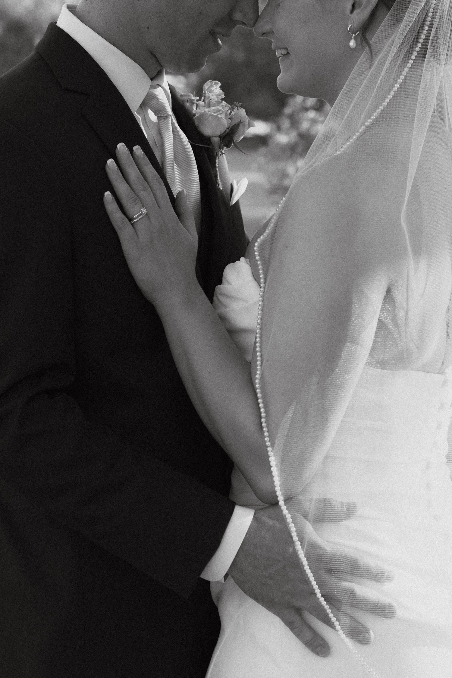 Black and white wedding photo showing intimate moment between bride and groom with veil and boutonniere detail.