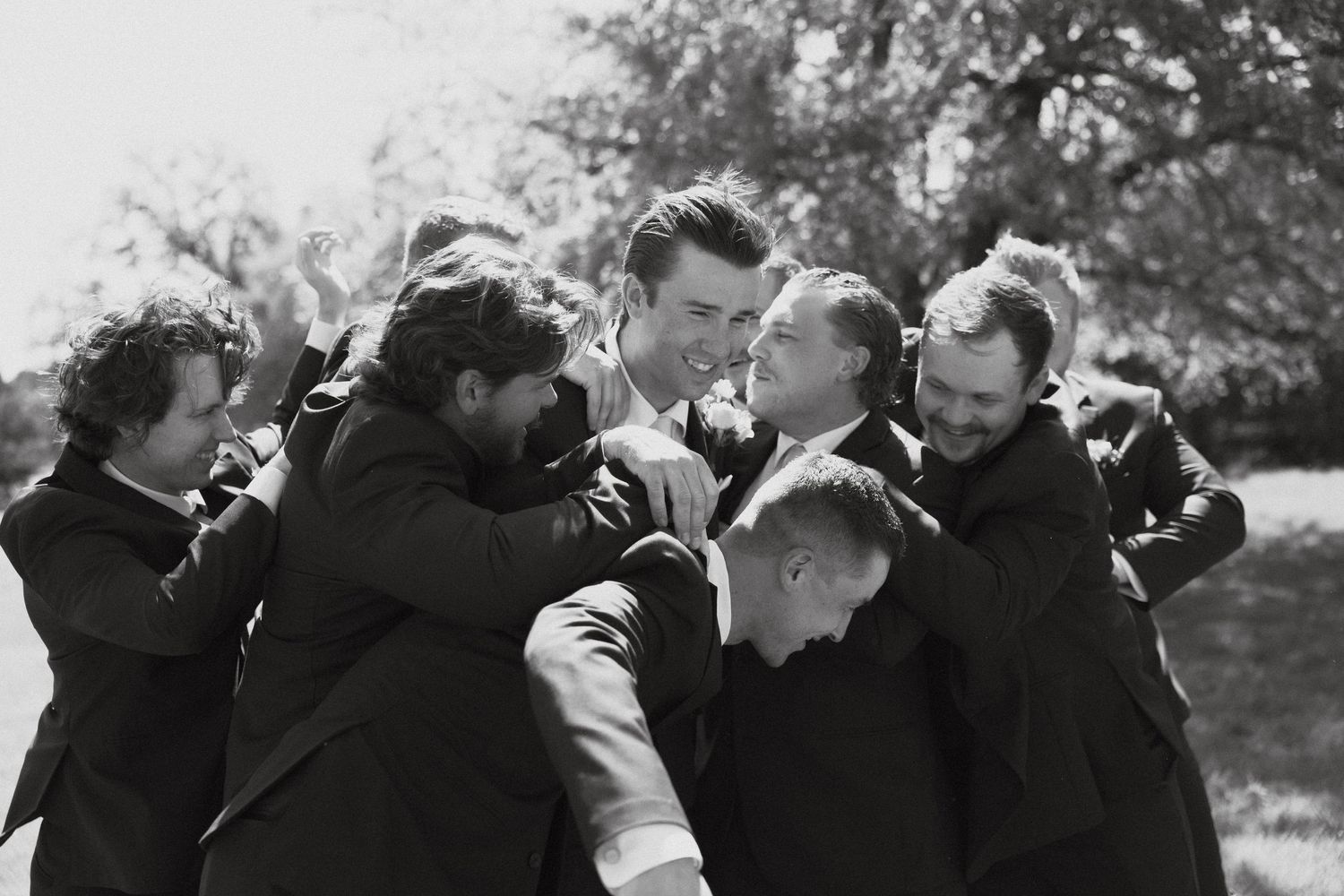 A black and white vintage photograph shows a group of people huddled together in conversation outdoors.
