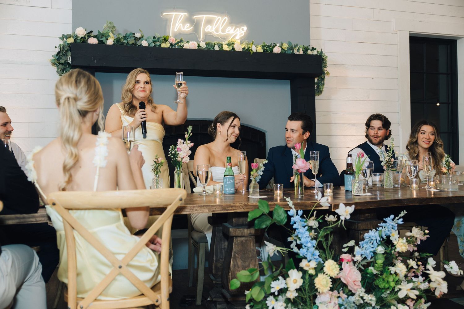 Wedding reception venue with floral arrangements and neon signage on gray and white walls.