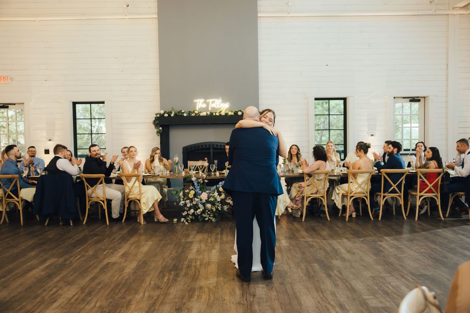 Wedding ceremony guests seated in rows inside an airy venue with large windows and white decor.