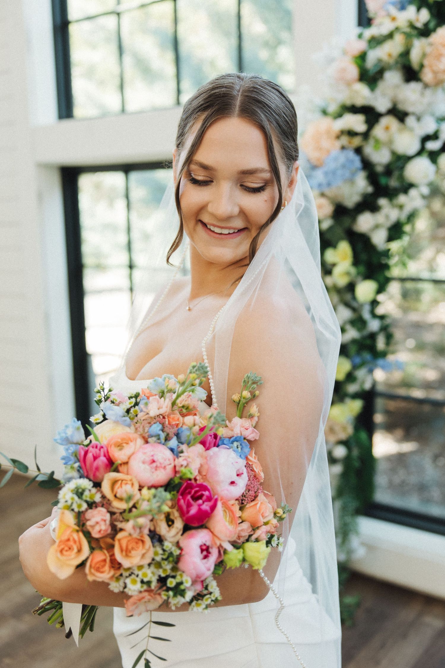 Beautiful wedding bouquet featuring pink roses, peach flowers and greenery in a natural sunlit setting.