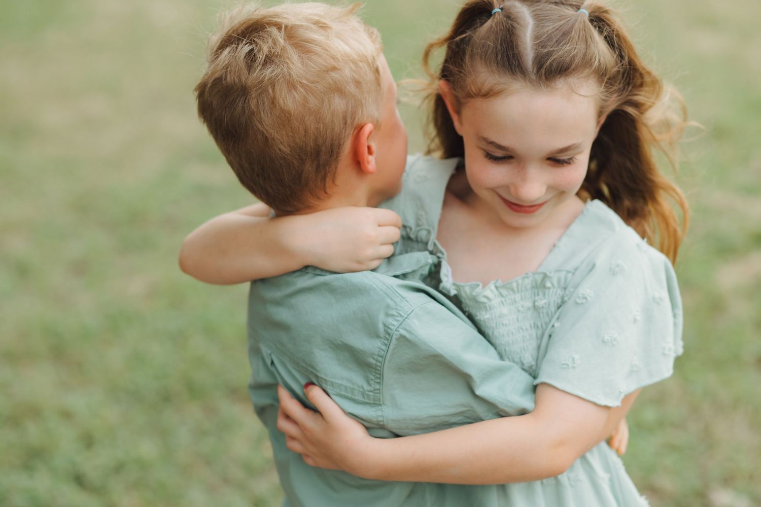 Sweet candid moments captured between siblings in casual outfits embracing outdoors in soft natural lighting.