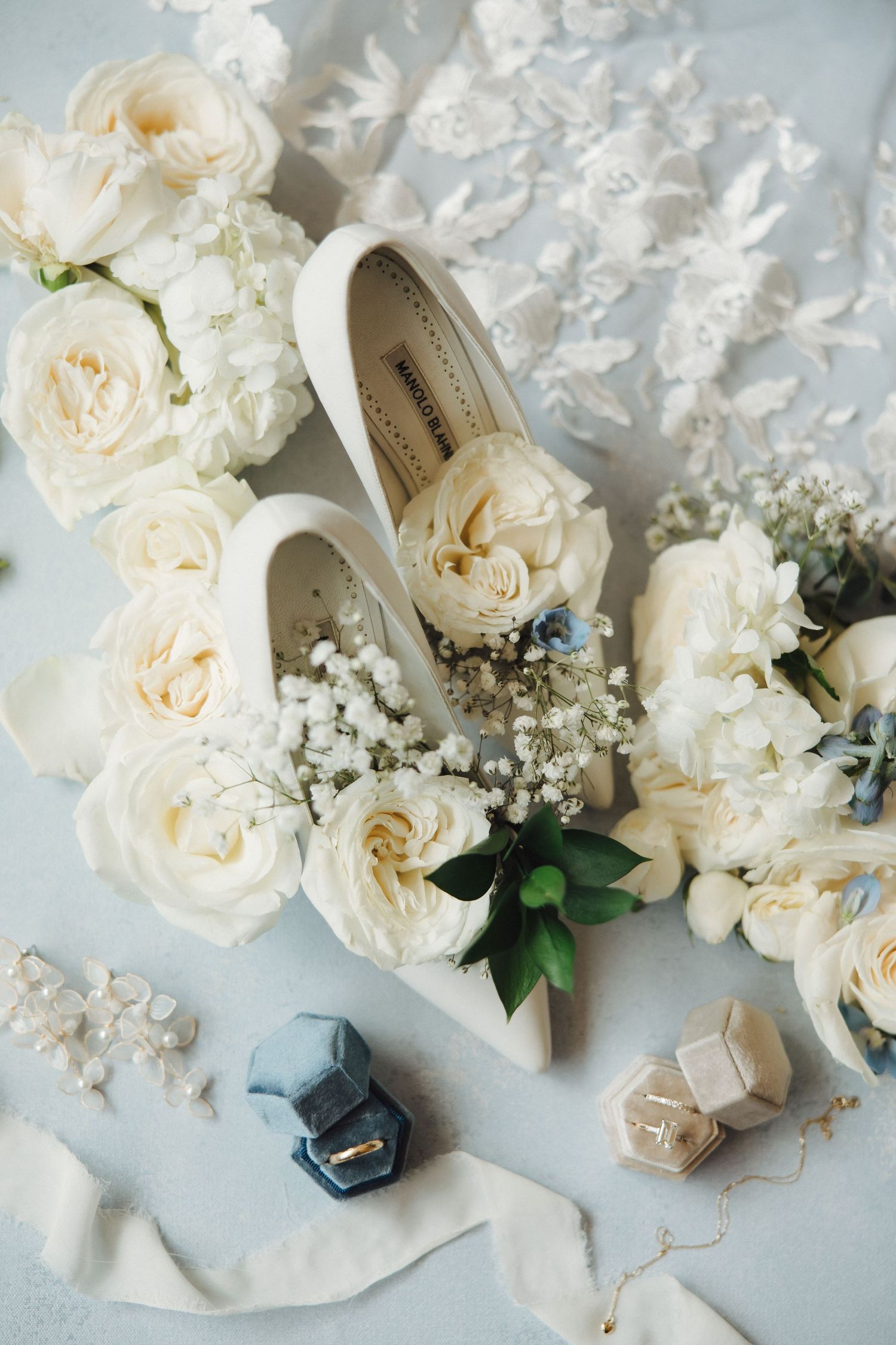 Wedding accessories including white roses, delicate baby's breath flowers, and decorative elements arranged on a light surface.