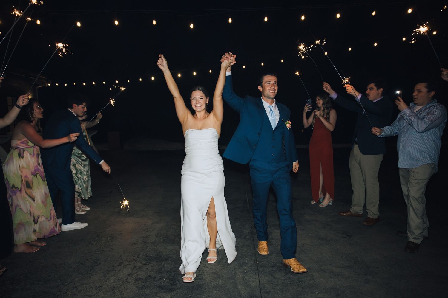 Wedding guests line up at night holding sparklers during a newlywed couple's joyful exit celebration.