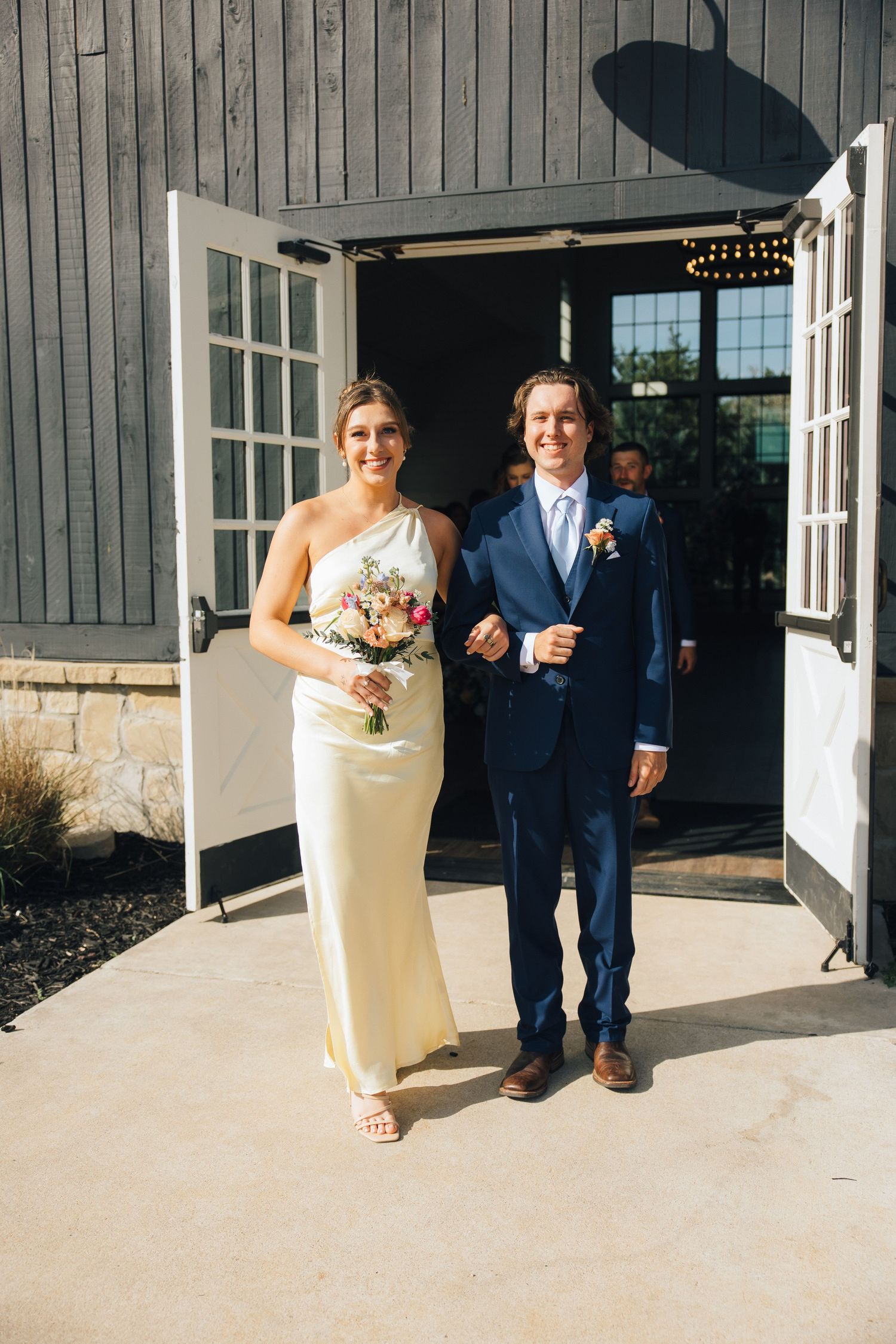 Wedding couple walking arm in arm through double doors of a rustic venue.
