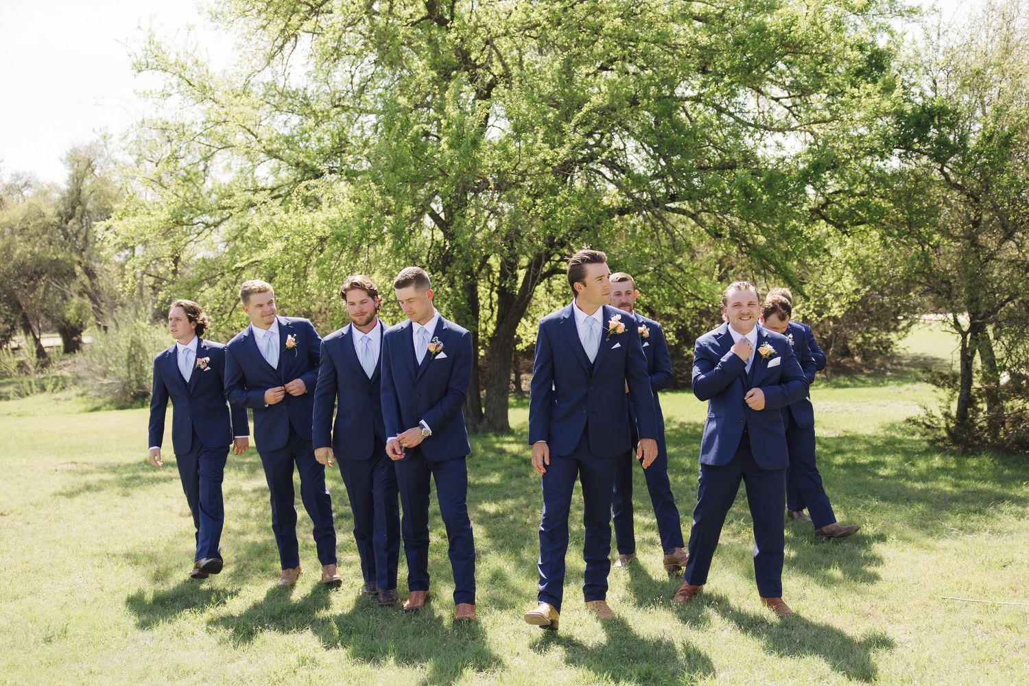 Group in navy blue suits stand together outdoors for photos in a natural garden setting.