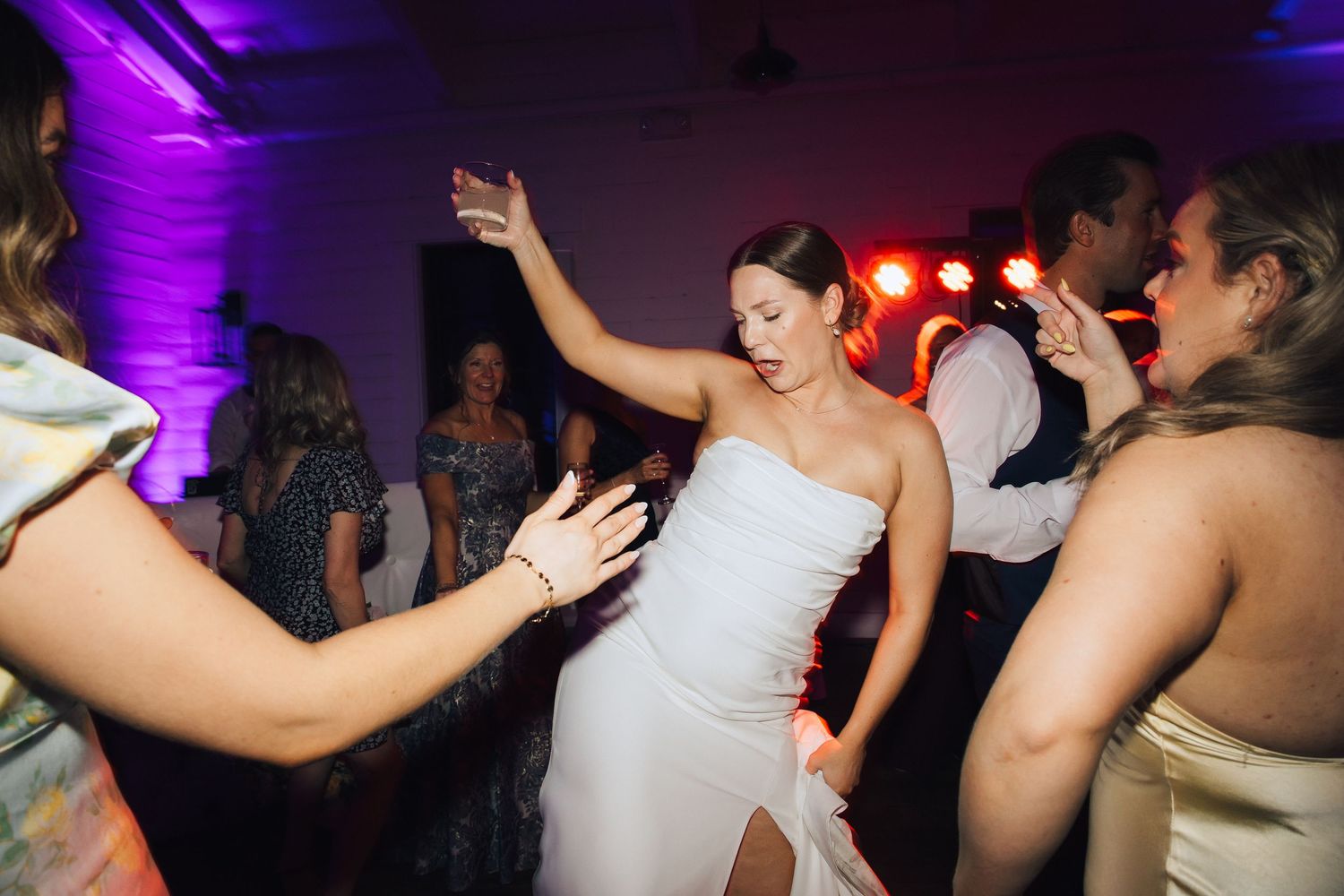 A person in a white wedding dress dances energetically on a dance floor illuminated by purple lighting.