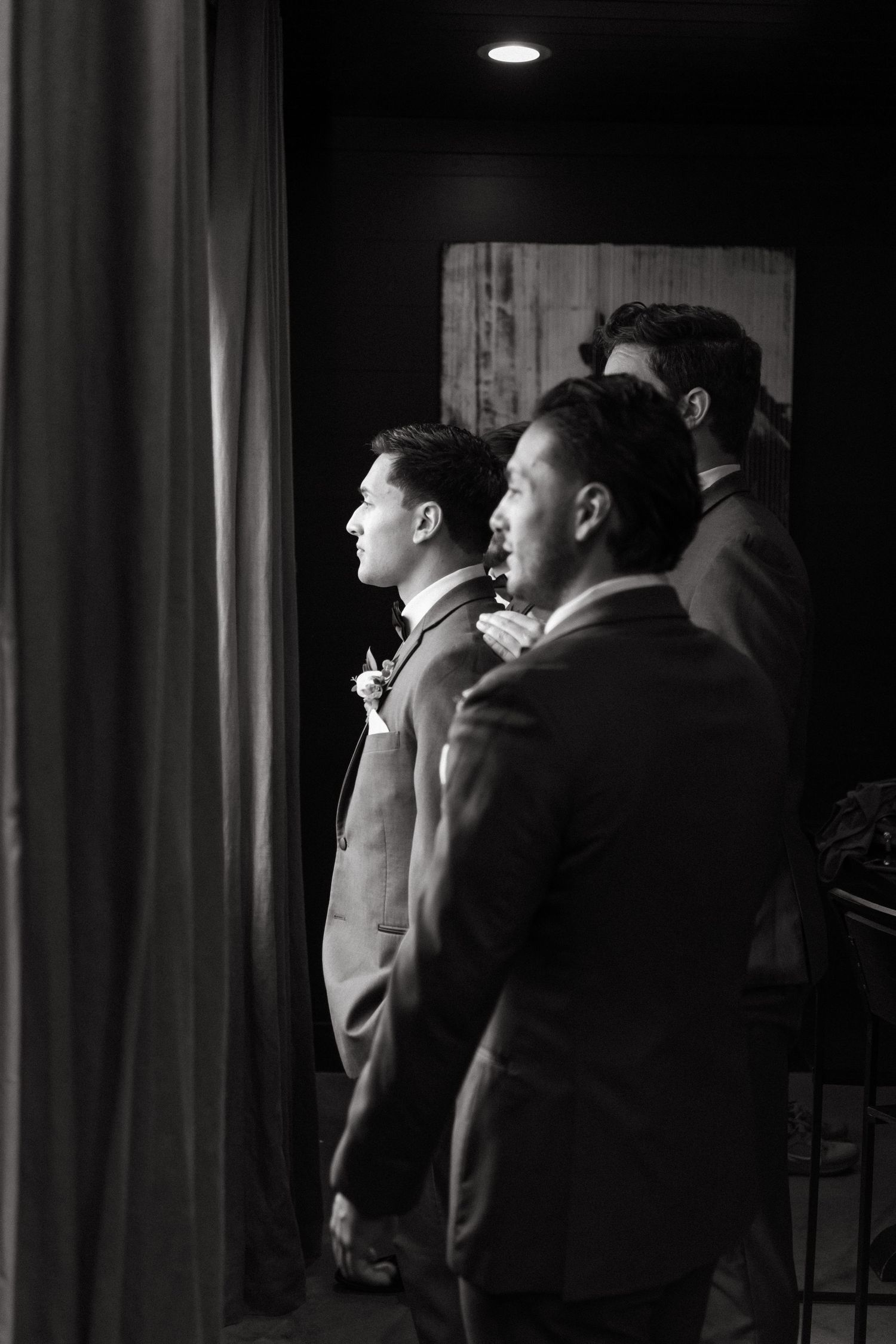 Black and white photo showing two men in suits standing beside a curtain, shot from profile view in what appears to be backstage.