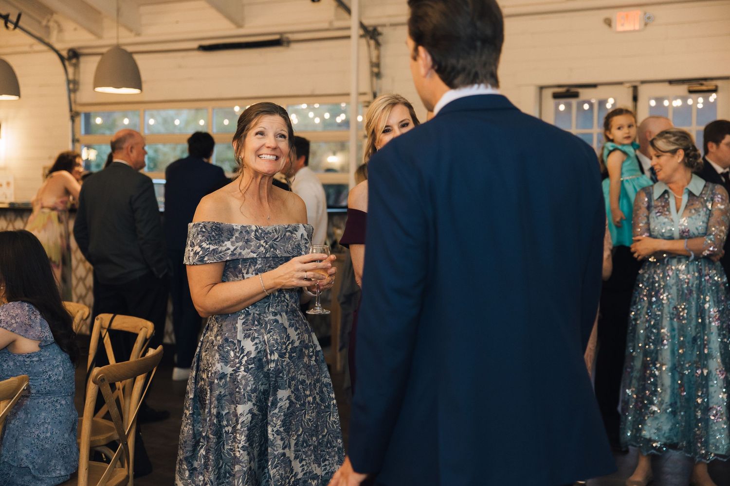 Wedding guests mingle and socialize during a reception in a bright indoor venue with rustic decor.