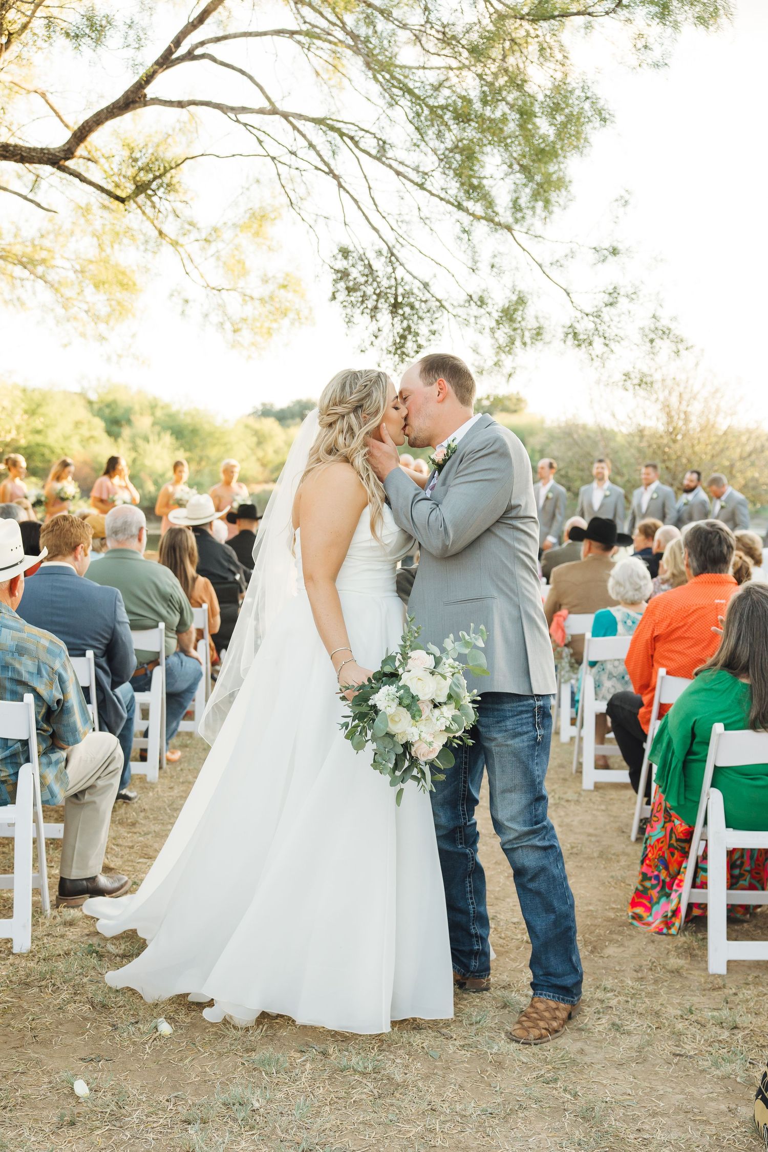 An outdoor wedding ceremony in a rustic setting with white chairs and natural lighting during golden hour.