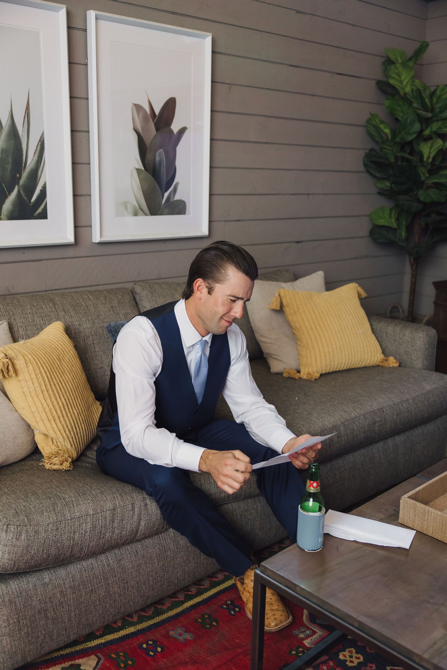 Person sitting on gray couch writing notes with yellow throw pillows and framed artwork on the wall.