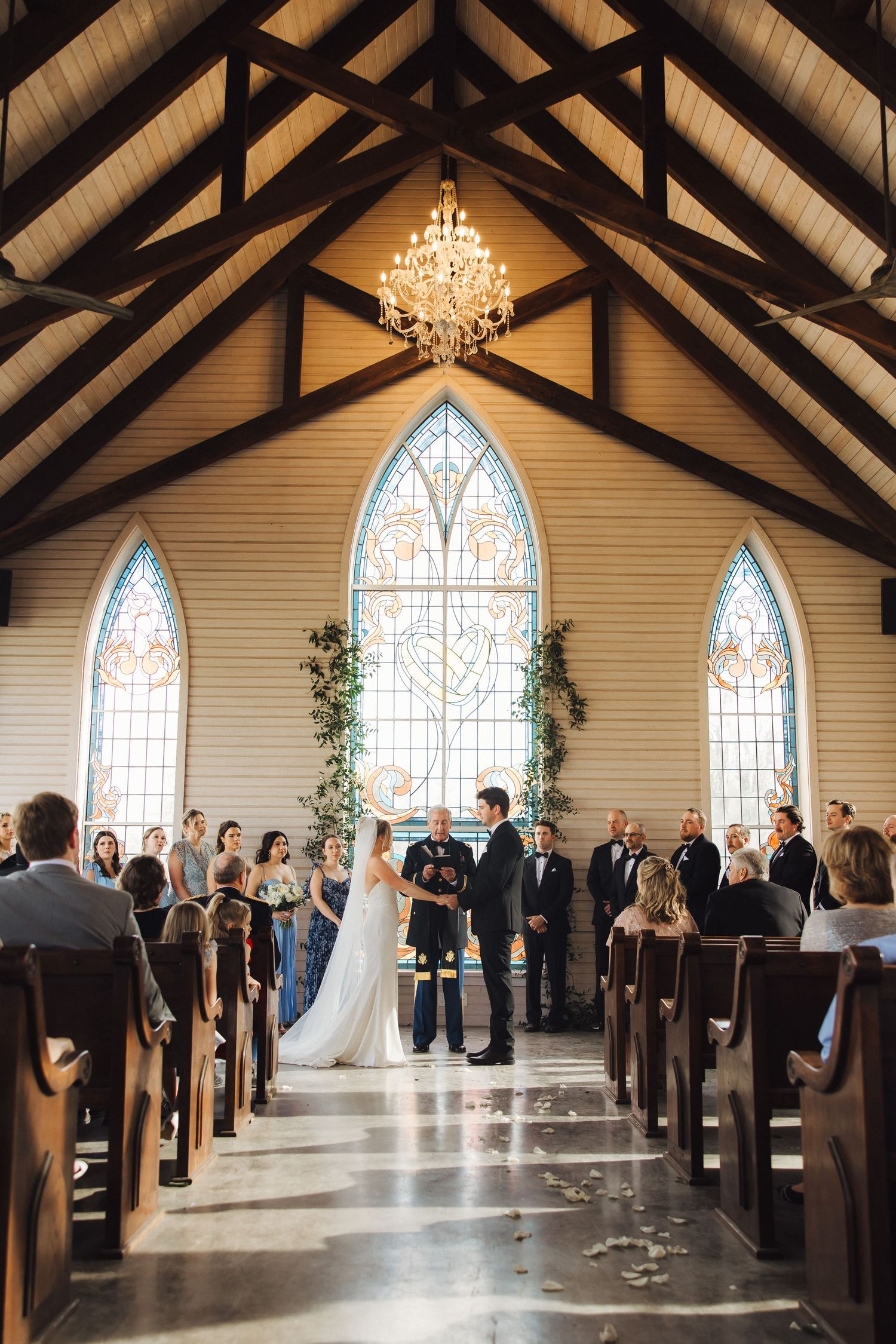 Wedding ceremony inside a chapel with vaulted wooden beams, stained glass windows and an elegant chandelier.