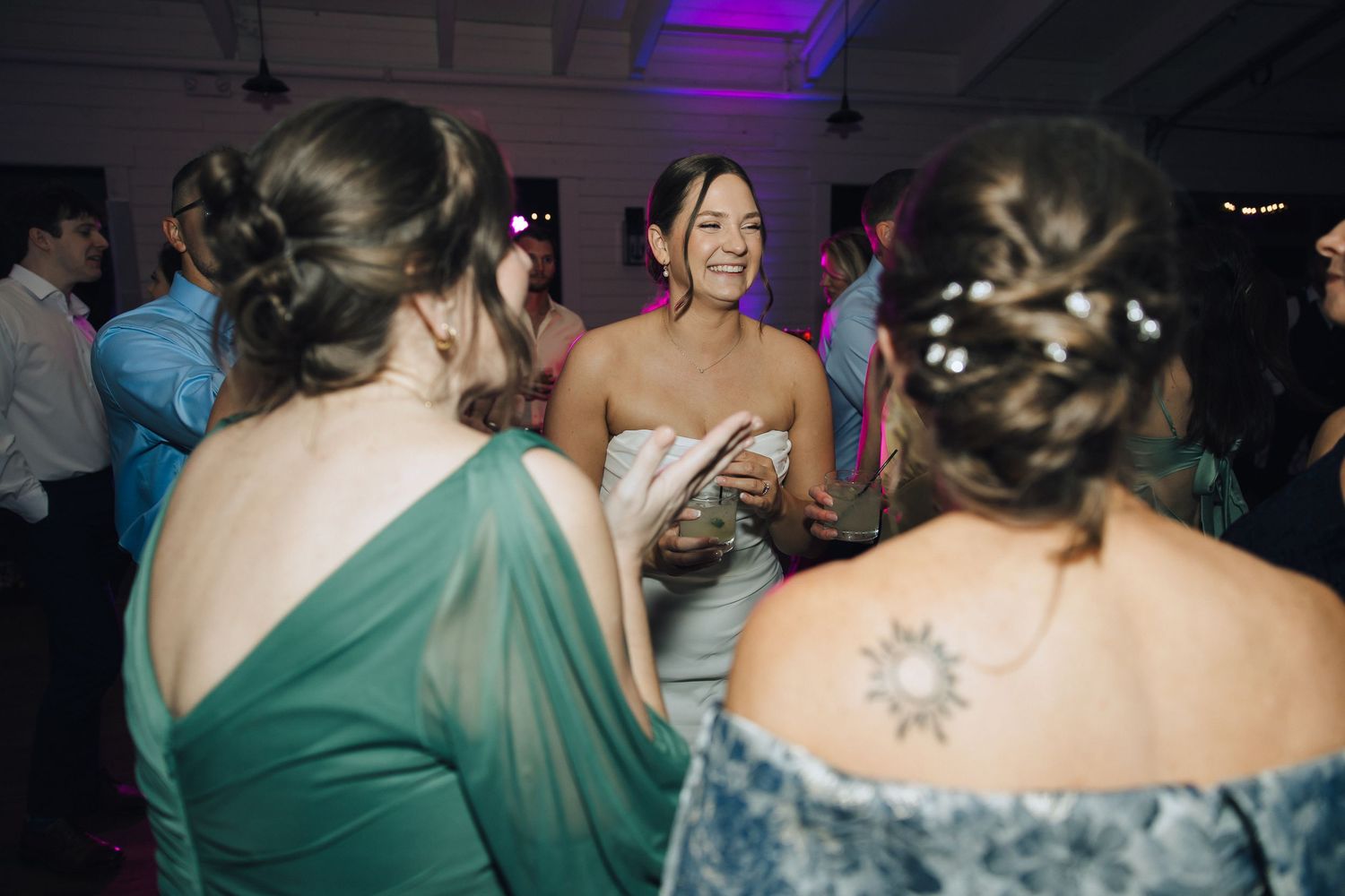 Groups of people dancing at a dimly lit party with purple lighting overhead.