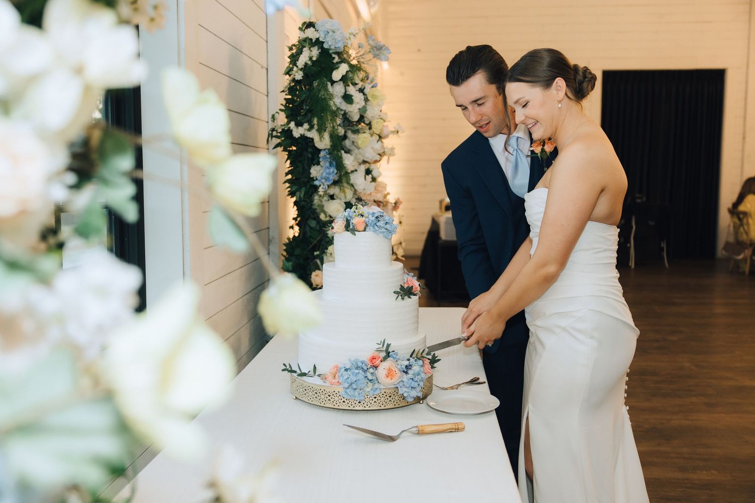 Couple signing documents at a wooden table during wedding ceremony with floral decorations.